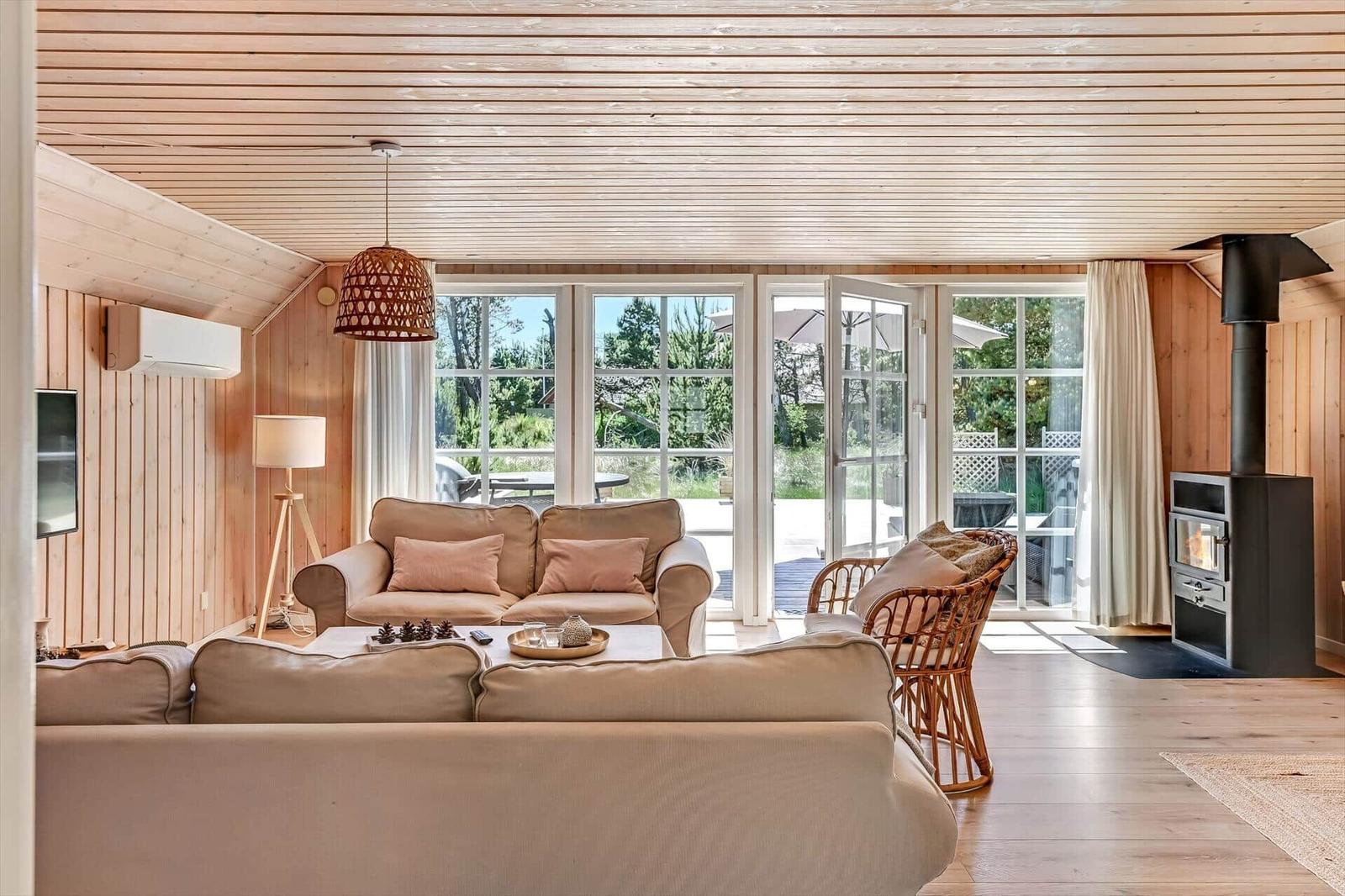 Wohnzimmer mit Holzdecke, Sofa, Kamin und Blick auf den Garten.