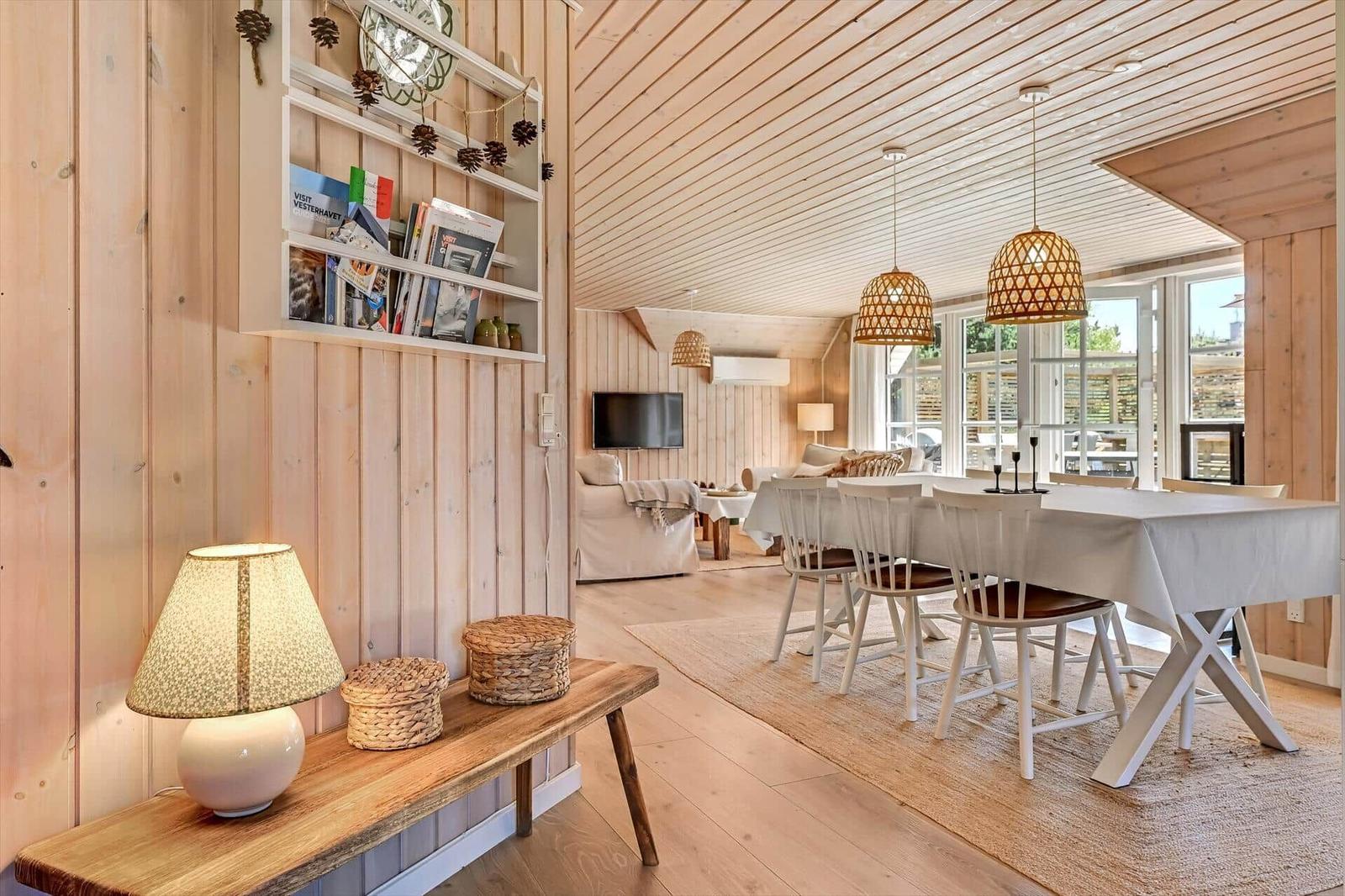 Wohn- und Essbereich mit Holzwand, Tisch, Stühlen und Lampe.