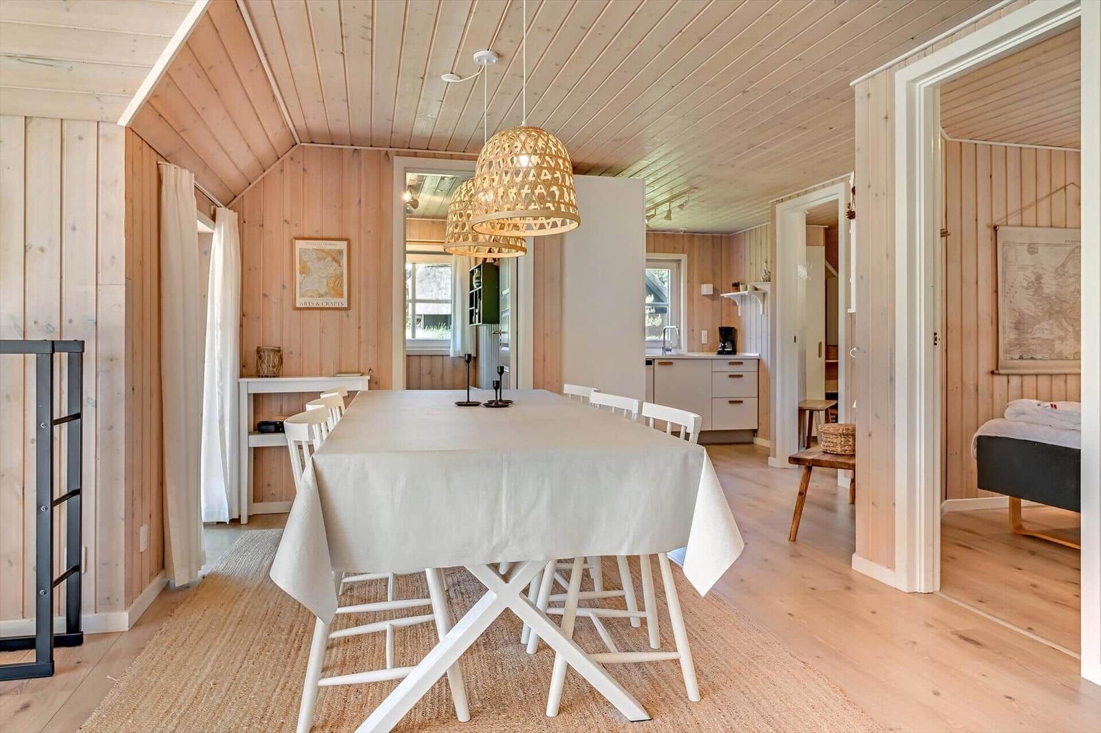 Esszimmer mit Tisch und Stühlen, Küche und Schlafzimmer im Hintergrund.