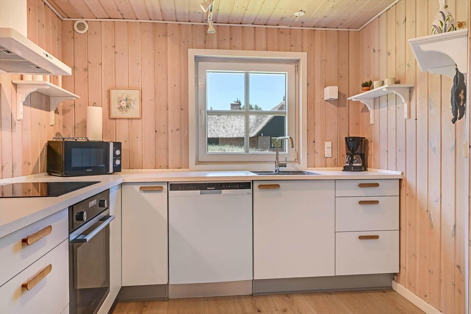 Küche mit Holzwand, Fenster, Spüle und weißen Schränken mit Holzgriffen.