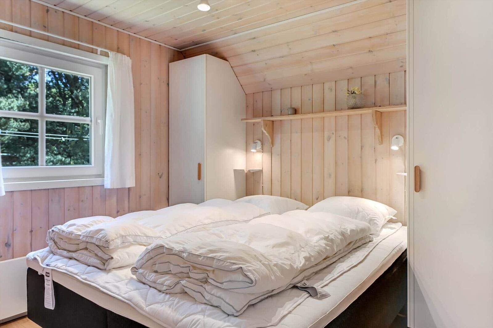 Schlafzimmer mit Bett, Fenster und Holzwand