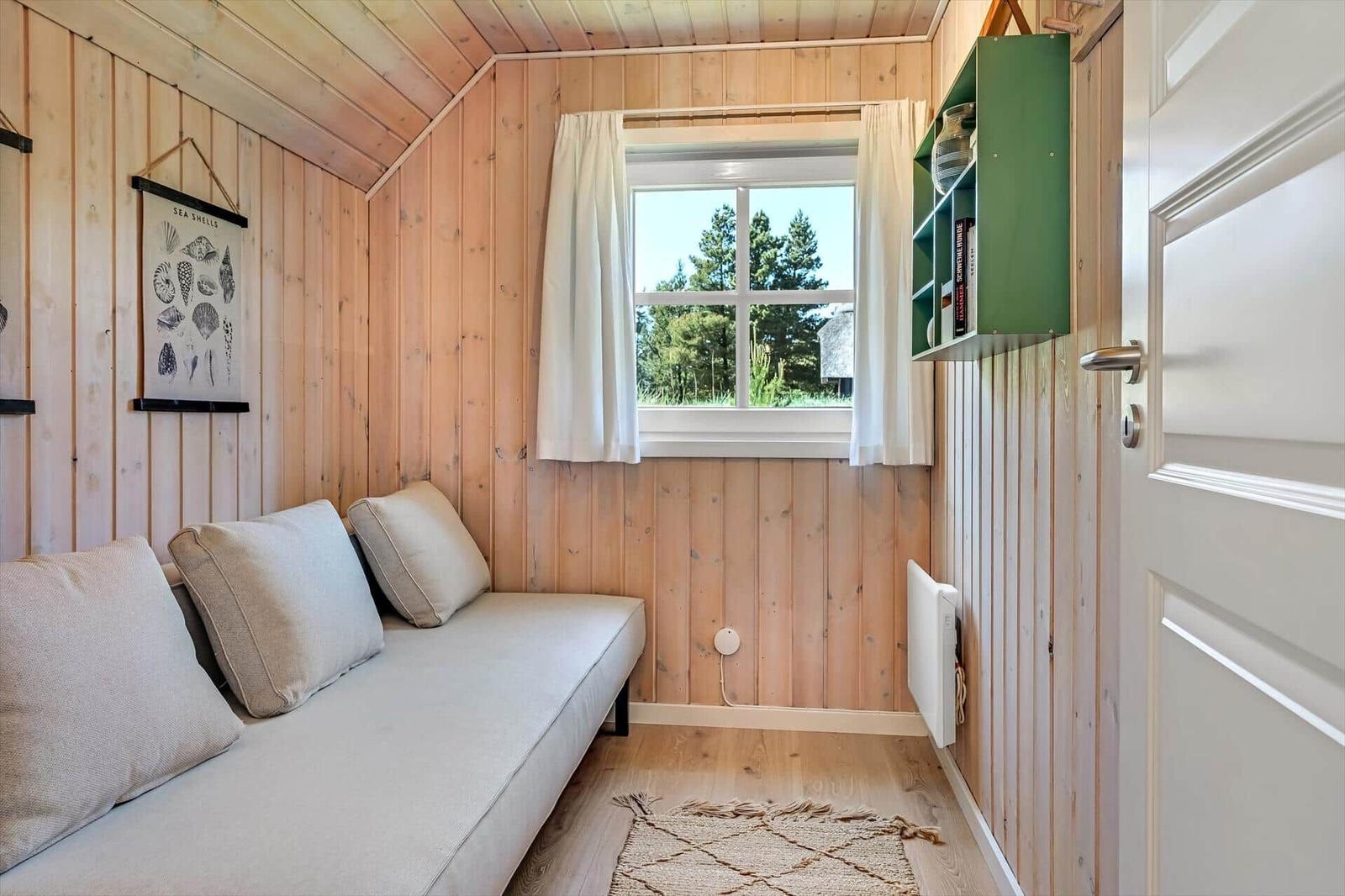 Ein Raum mit Holzwänden, Sofa, Fenster und grünem Regal.