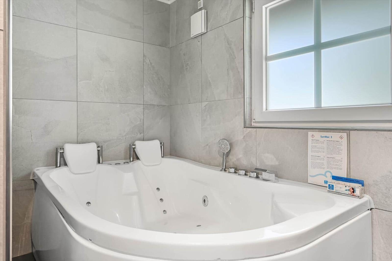 Eine große Whirlpool-Badewanne mit Kopfstützen und Duschkopf an der Wand.