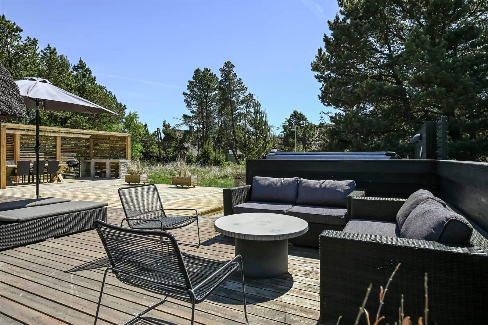 Terrasse mit Sitzgruppe, Tisch und Sonnenschirm. Hintergrund: Wald und Grillbereich.