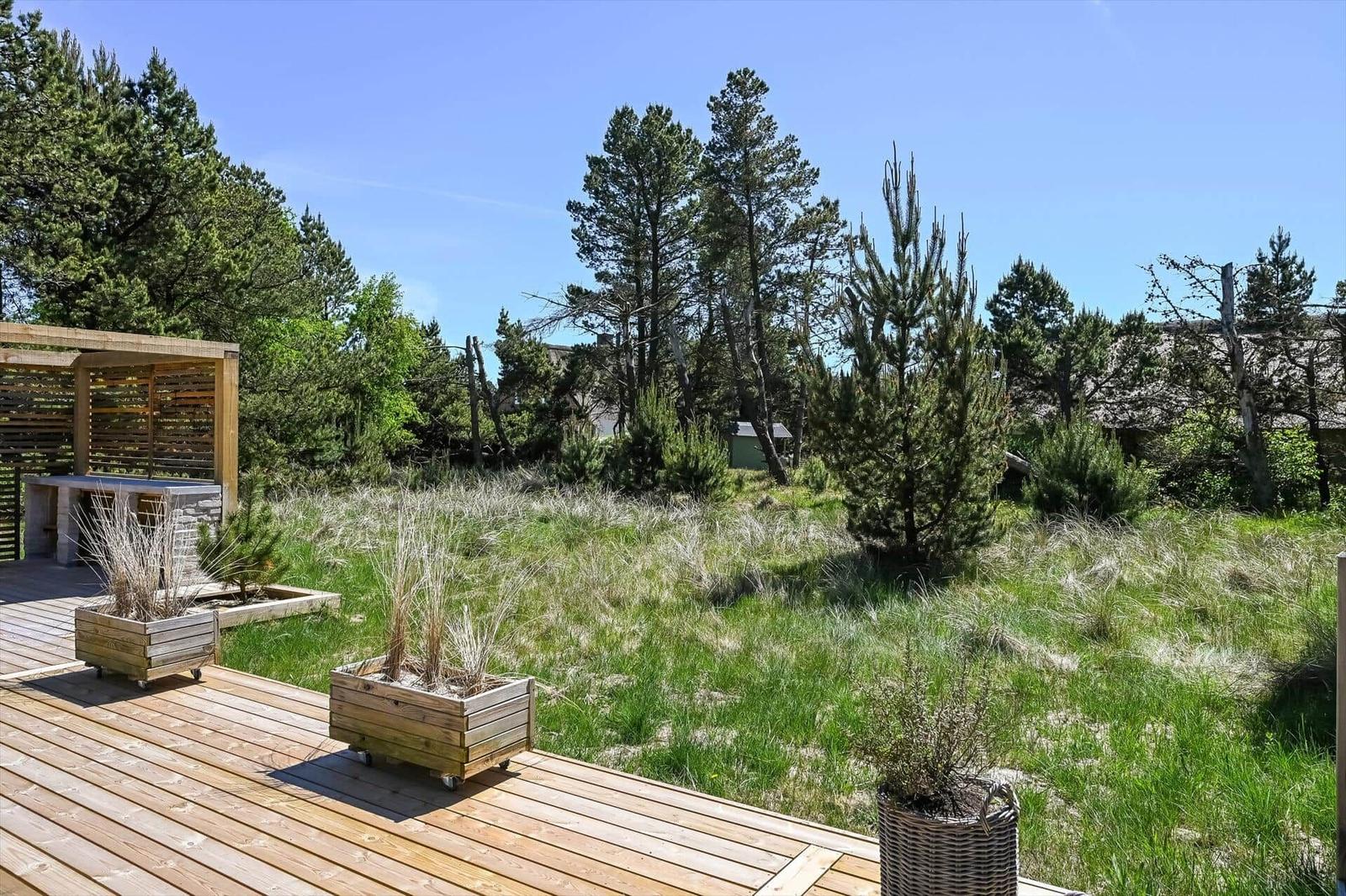 Holzterrasse mit Pflanzenkästen und Blick auf grünen Garten mit Bäumen.
