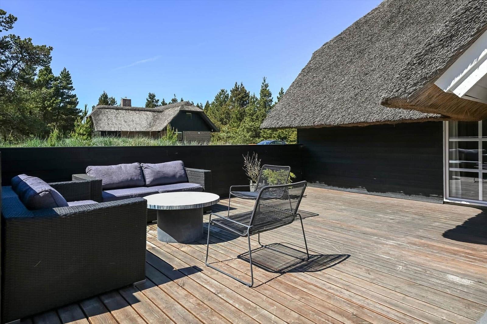 Terrasse mit Sitzgruppe, Tisch und Blick auf strohgedeckte Häuser.