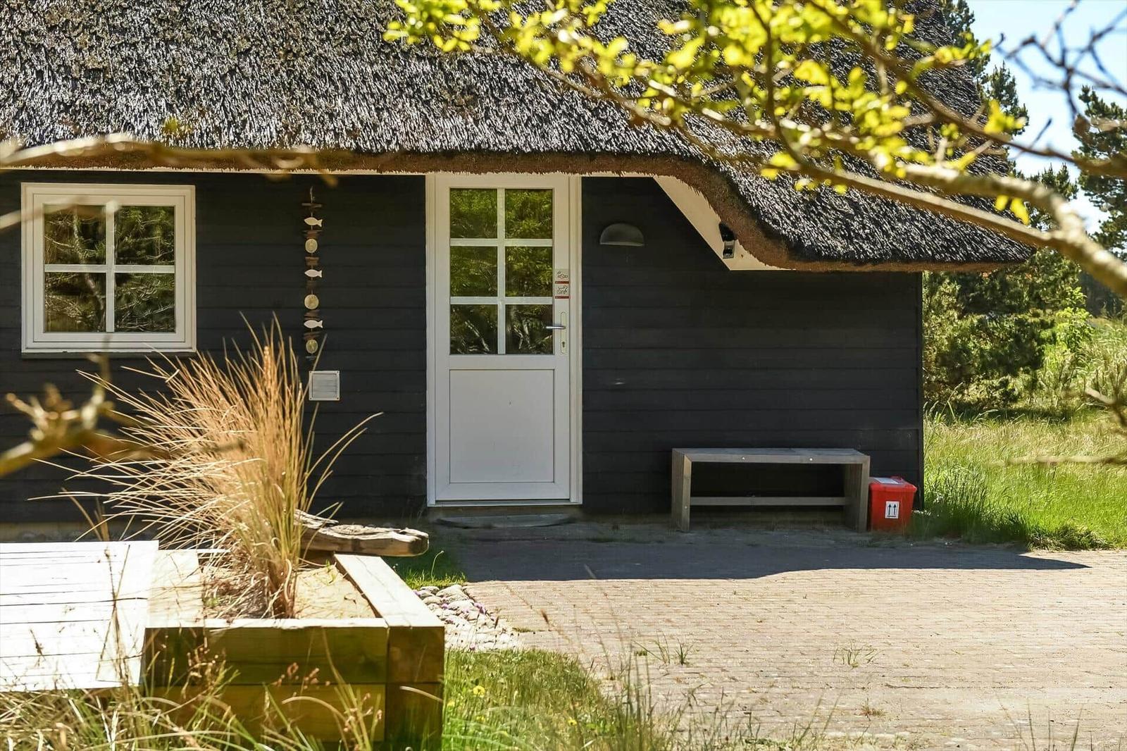 Schwarzes Holzhaus mit Strohdach, weißer Tür und Bank vorne.