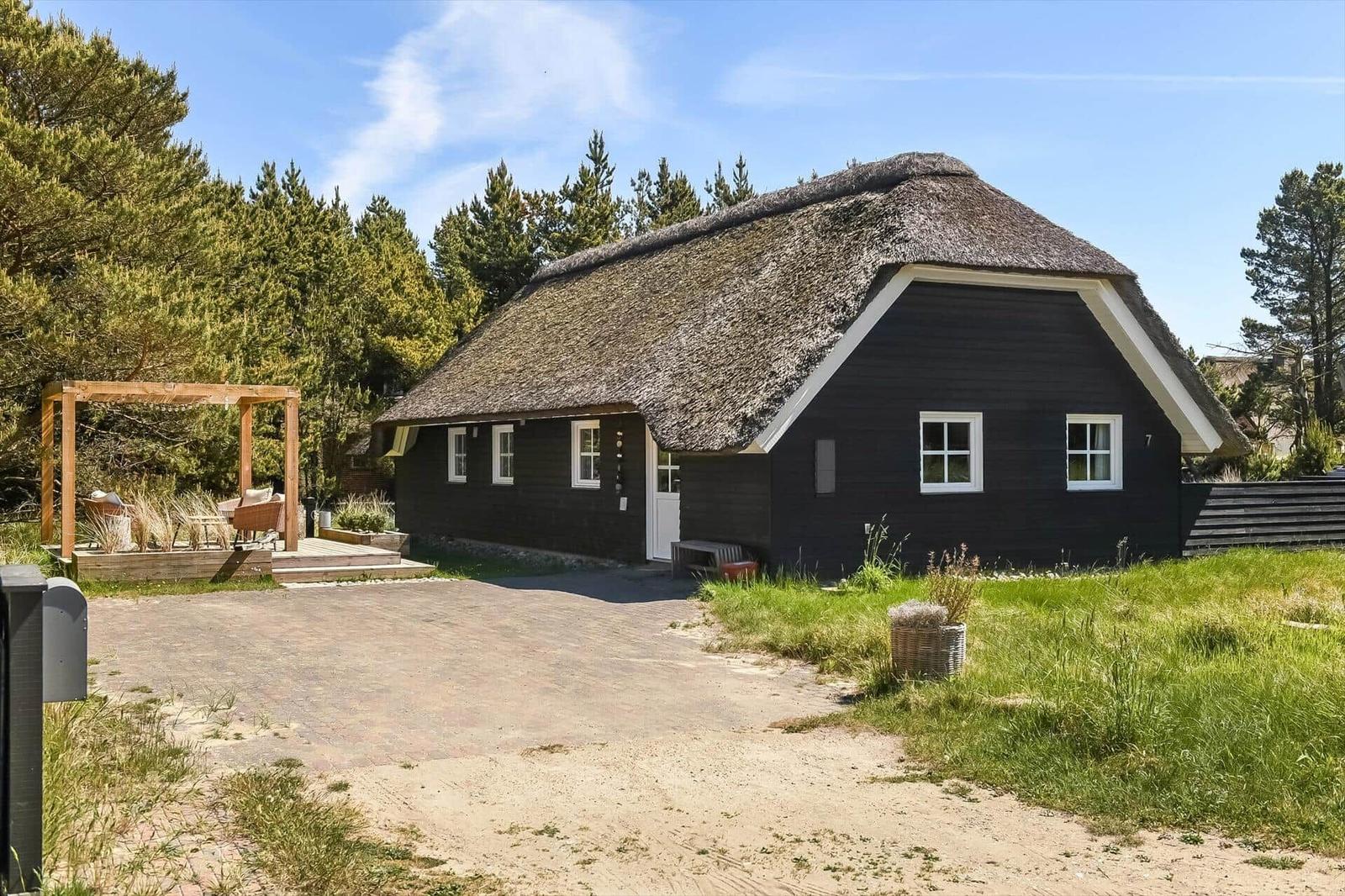 Schwarzes Strohdachhaus mit weißem Fensterrahmen und Holzterrasse im Grünen.