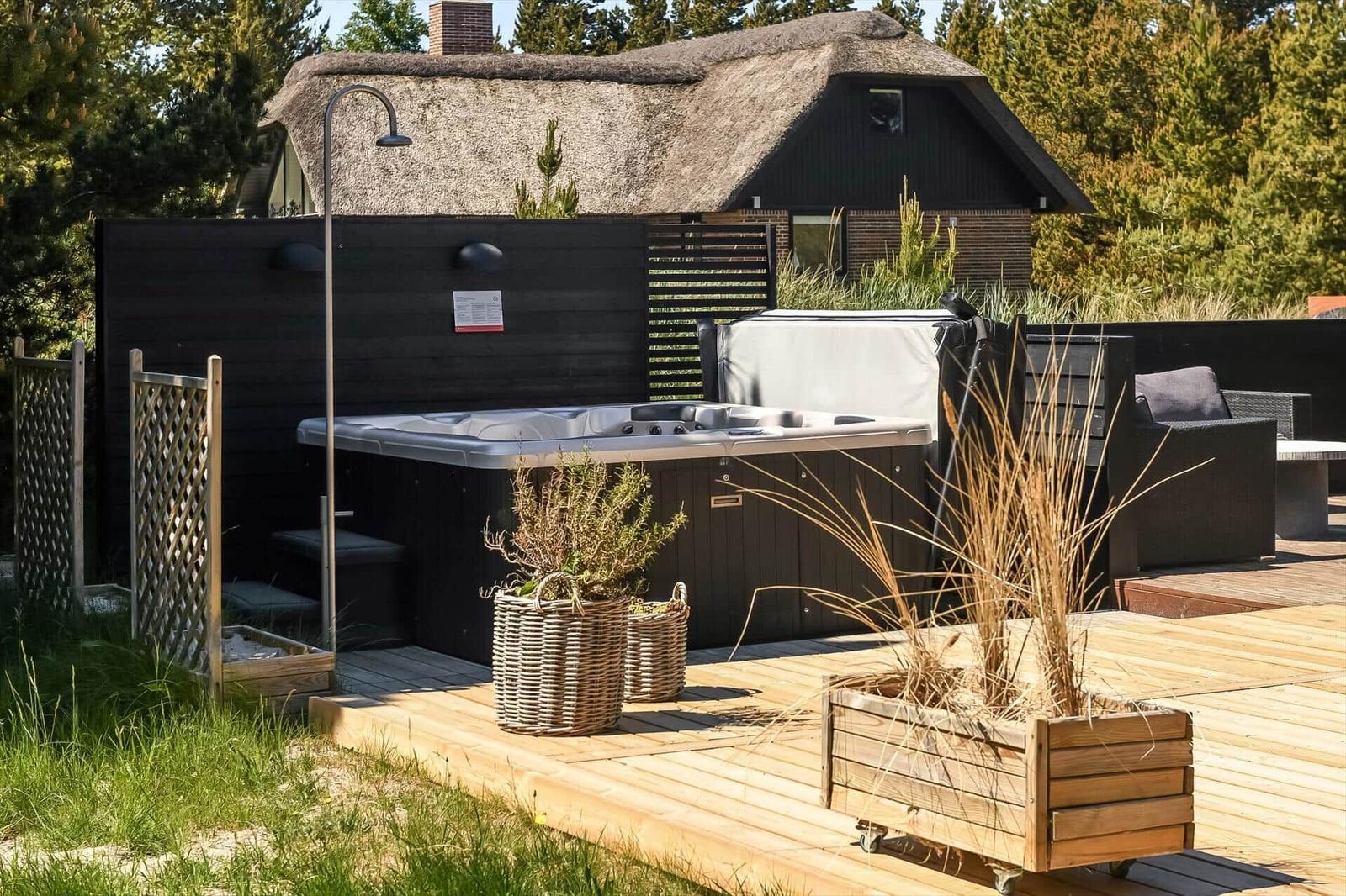 Hochwertige Außenterrasse mit Whirlpool, Pflanzen und Gartenmöbeln vor einem schwarzgedeckten Haus.