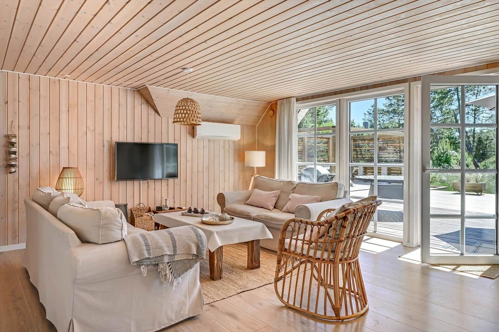 Wohnzimmer mit Holzwand, Sofa, Fernseher und Blick auf die Terrasse.