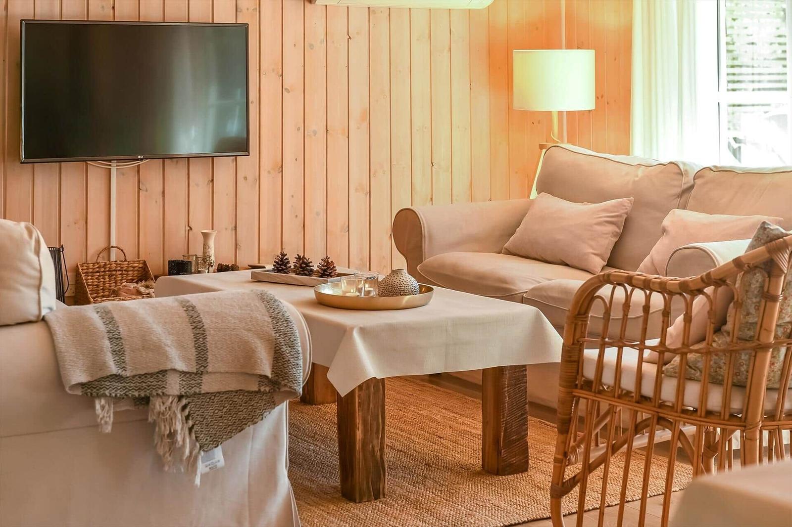 Wohnzimmer mit Sofa, Couchtisch und Fernseher an Holzwand.