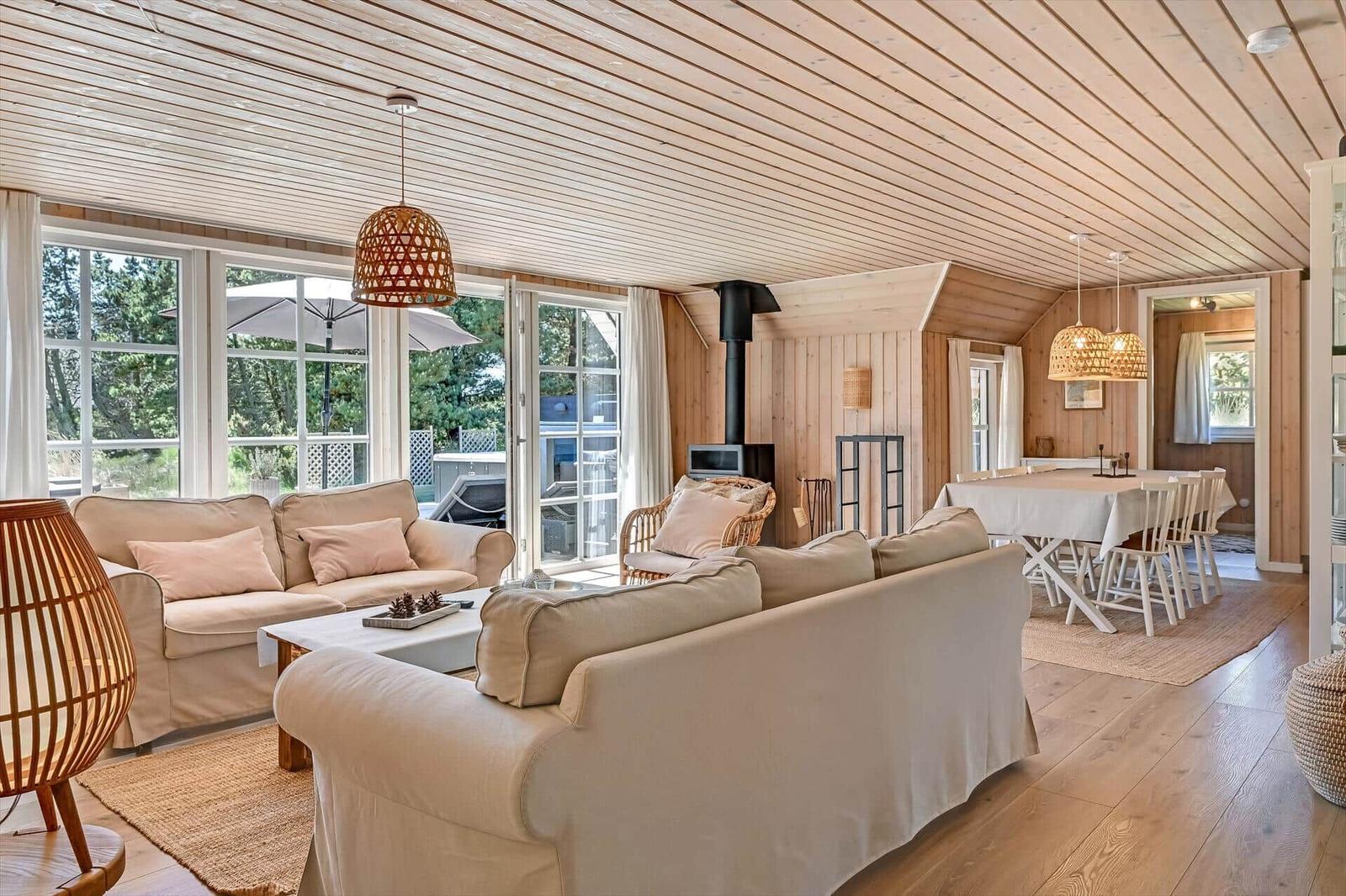 Wohn- und Essbereich mit Holzdecke, Sofas und Tisch. Durchgang zur Küche.