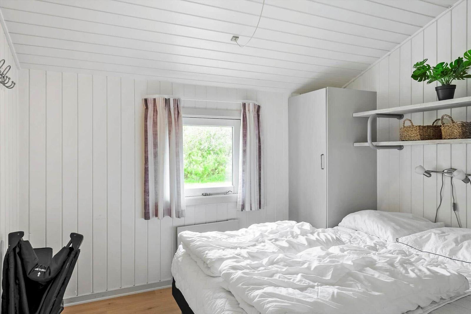 Schlafzimmer mit weißer Bettwäsche, Fenster mit Vorhängen und Schrank.
