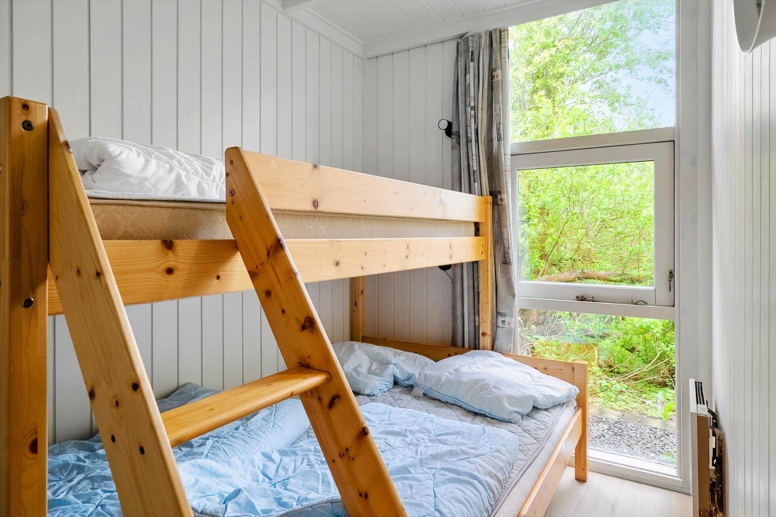 Ein Schlafzimmer mit Holzbett und Fensterblick auf grüne Bäume.