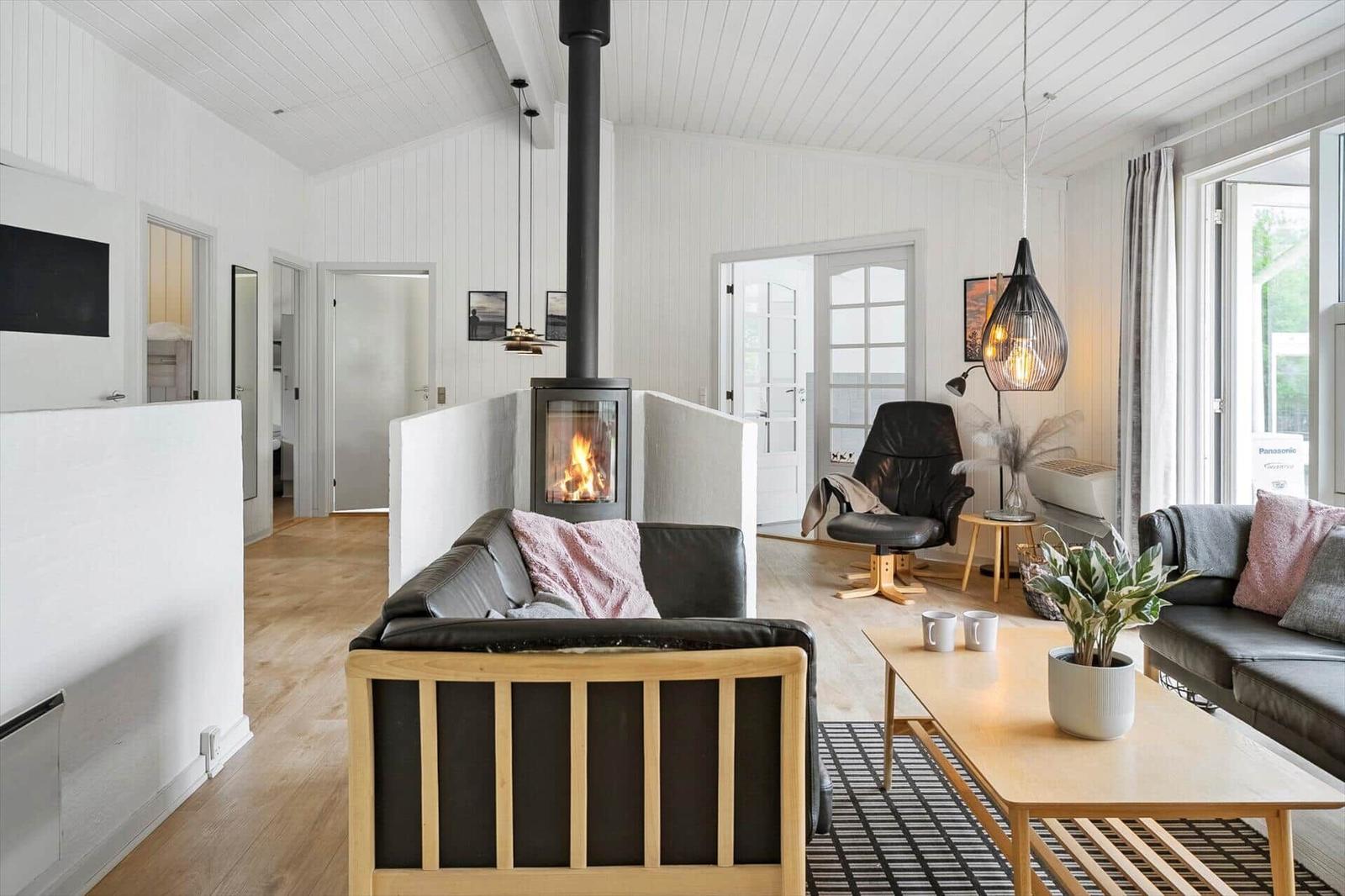 Wohnzimmer mit Kamin, Ledersofa und Holztisch. Weiße Wände und Holzboden.