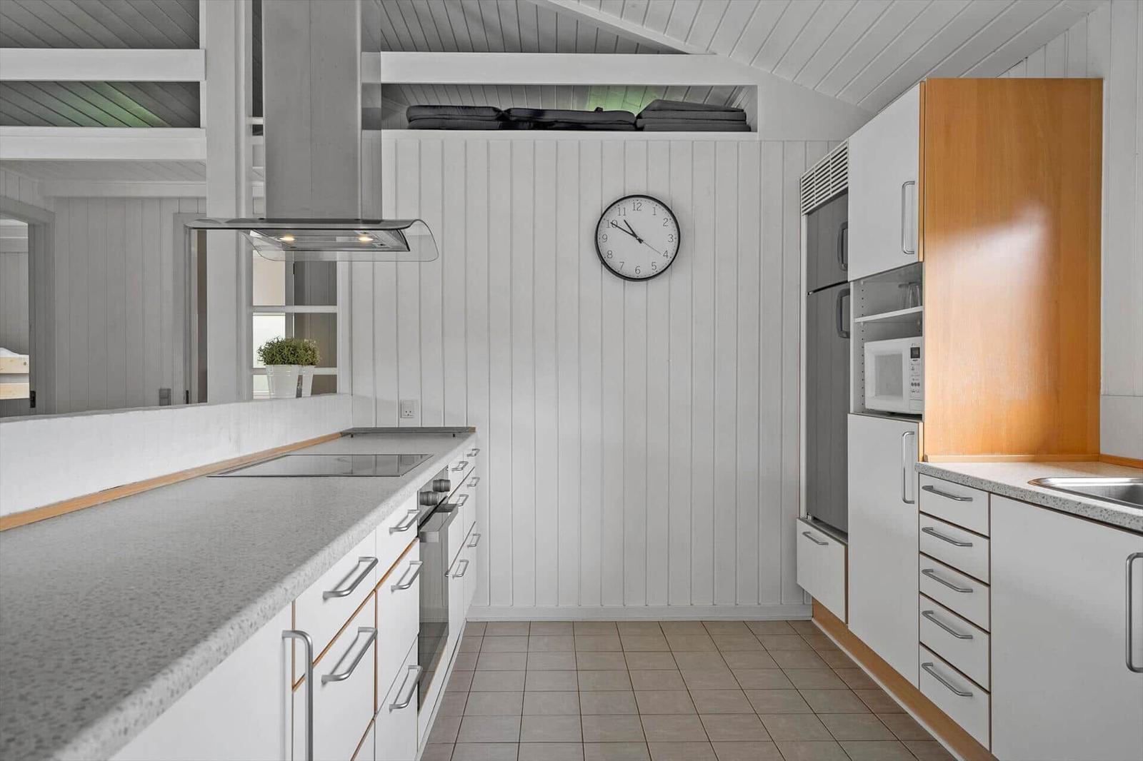 Moderne Küche mit weißen Schränken, Edelstahlgeräten und Holzelementen an der Wand.