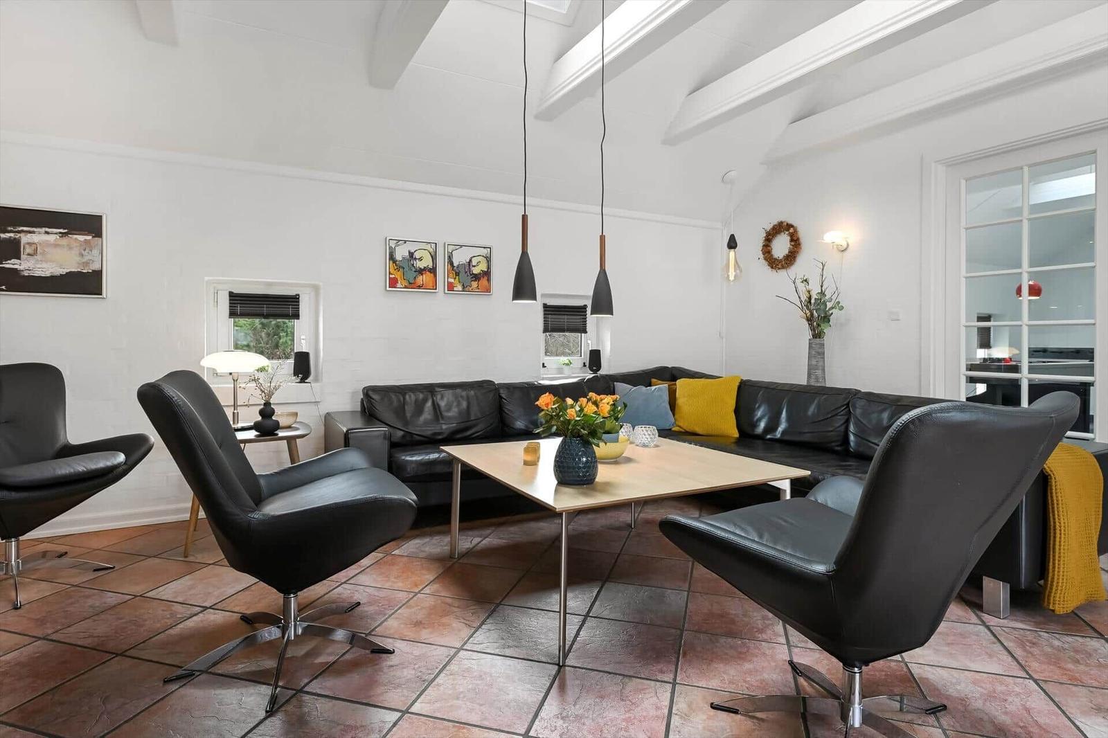 Ein Wohnzimmer mit schwarzem Sofa, drei Stühlen und einem Holztisch.