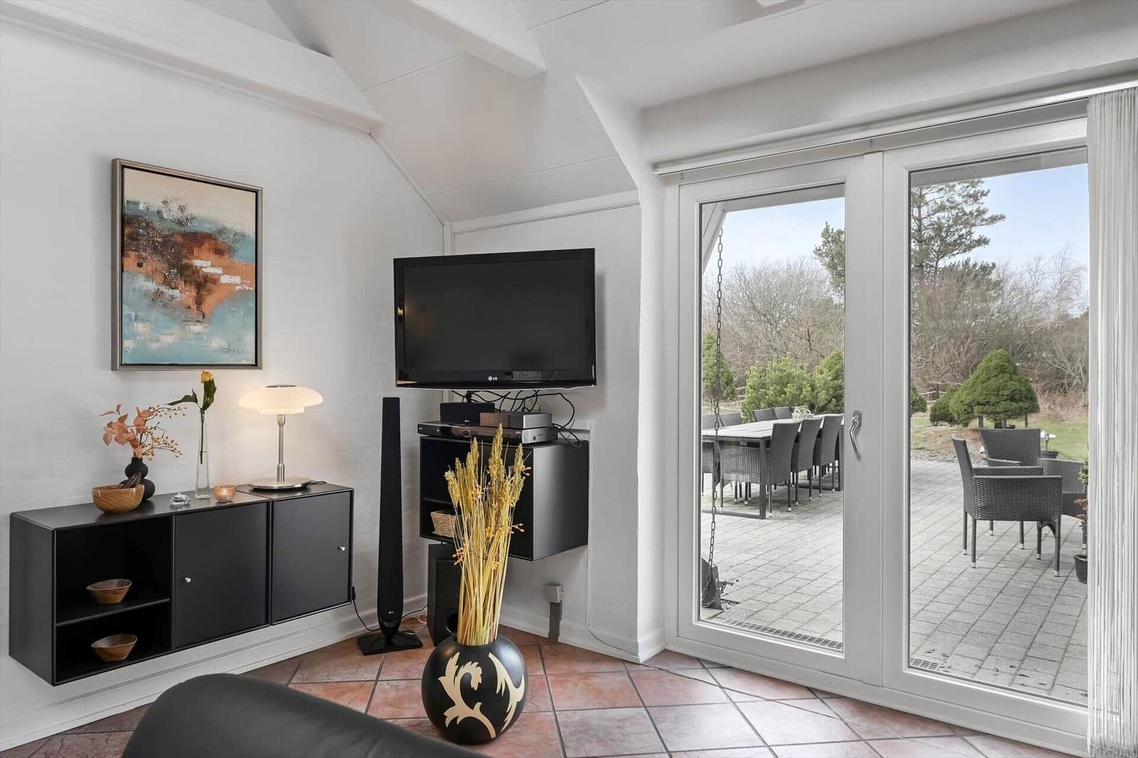 Wohnzimmer mit TV, Schwebetüren und Terrasse mit Gartenmöbeln.