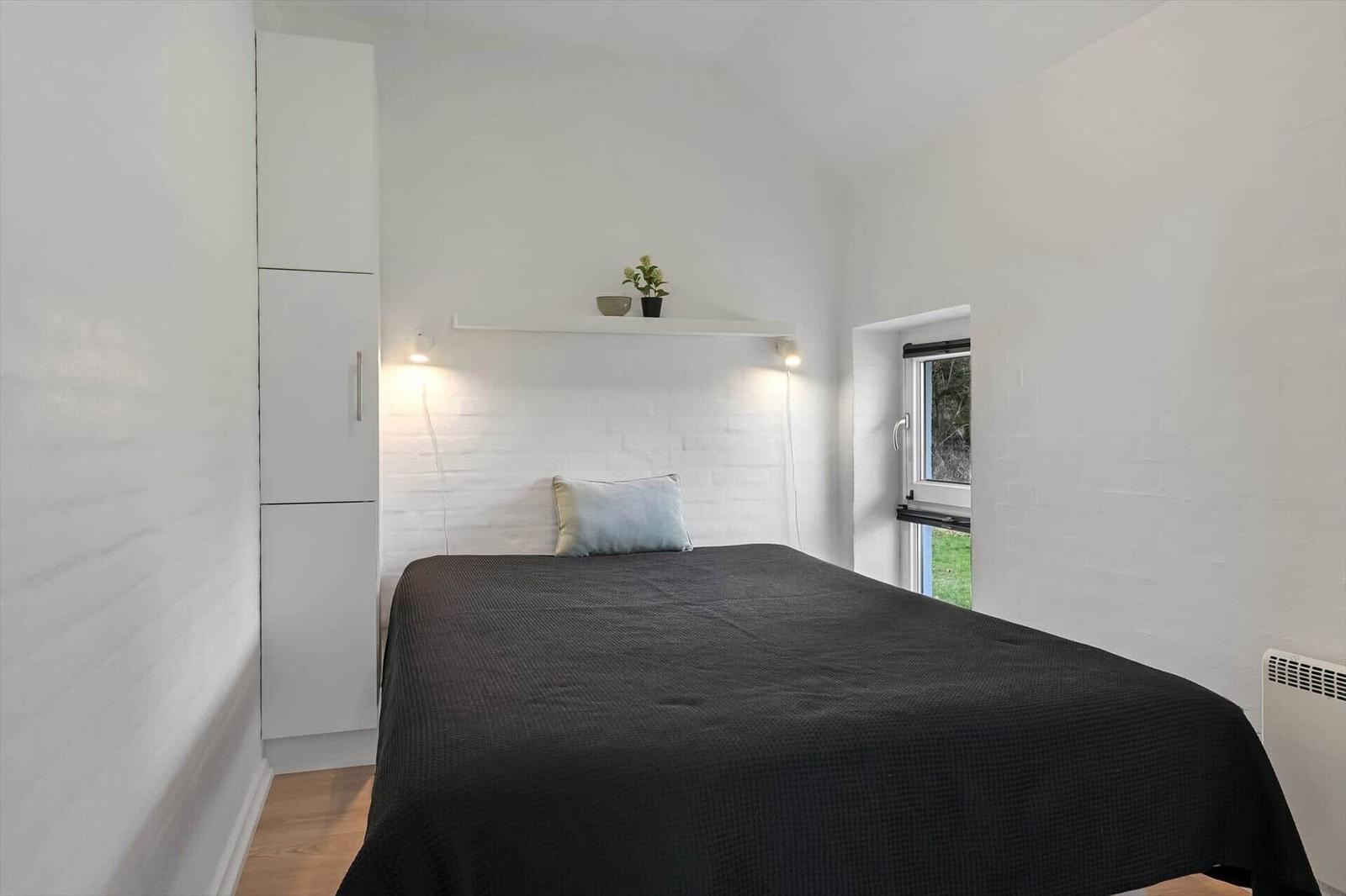 Schlafzimmer mit Bett, Schrank und Fenster. Wandregal mit Pflanze und Beleuchtung.