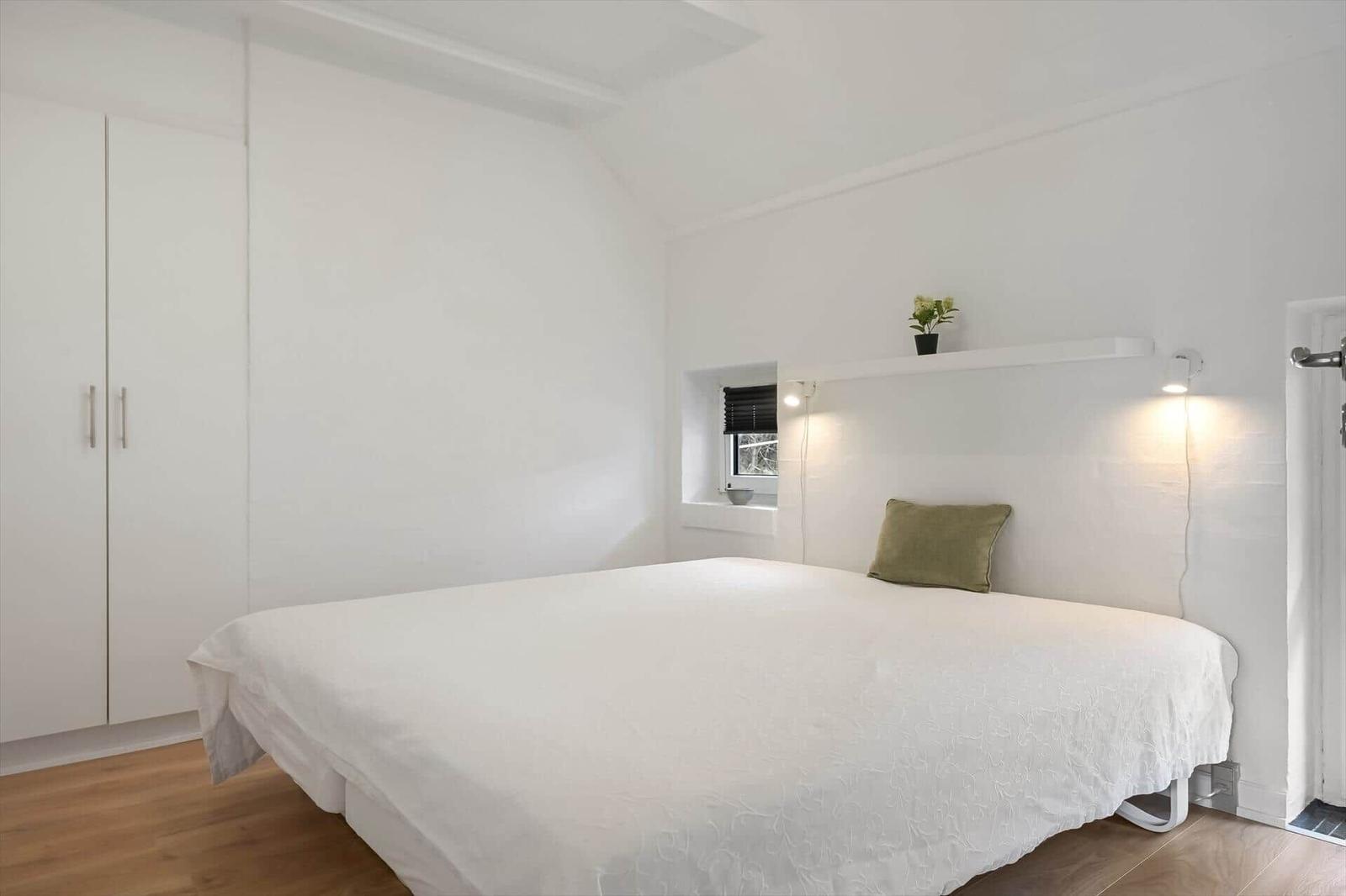 Schlafzimmer mit weißem Bett, Kleiderschrank und Fenster