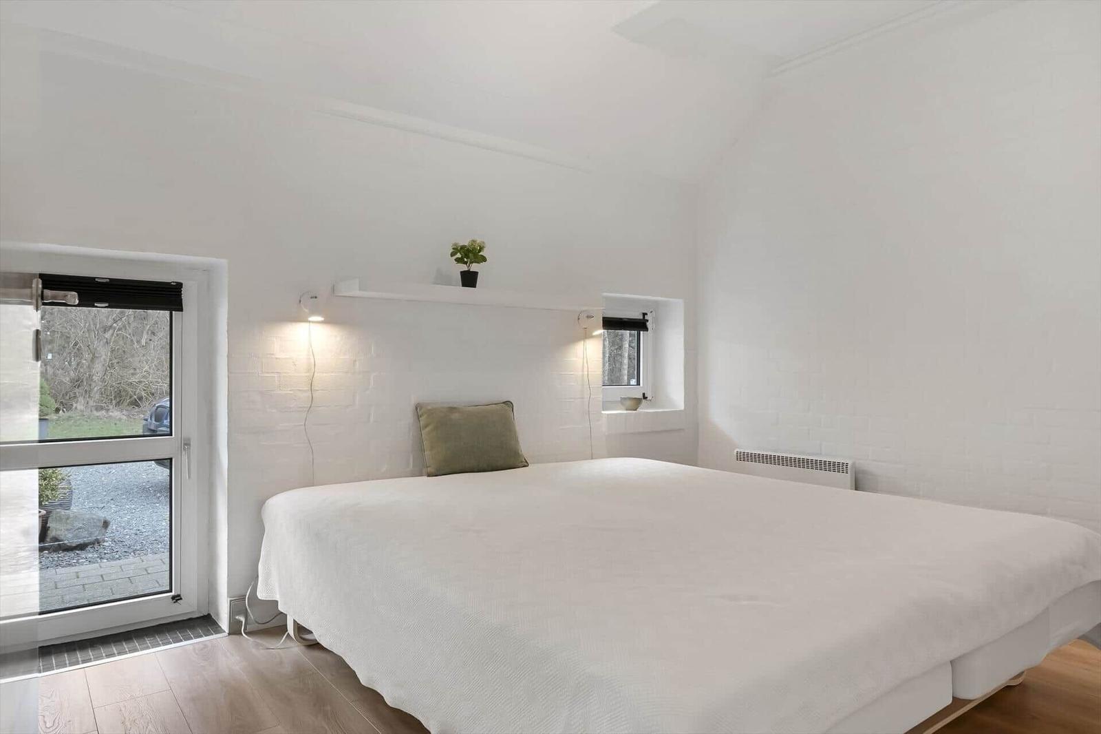 Schlafzimmer mit Bett, Fenster und Wandregal. Weiße Wände und Holzboden.