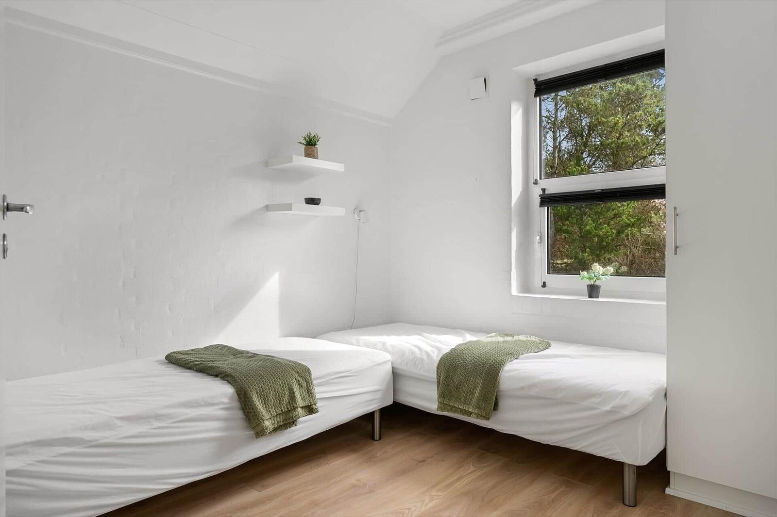 Zwei Einzelbetten mit grünen Decken, Fenster mit Blick auf Bäume und weiße Wände.