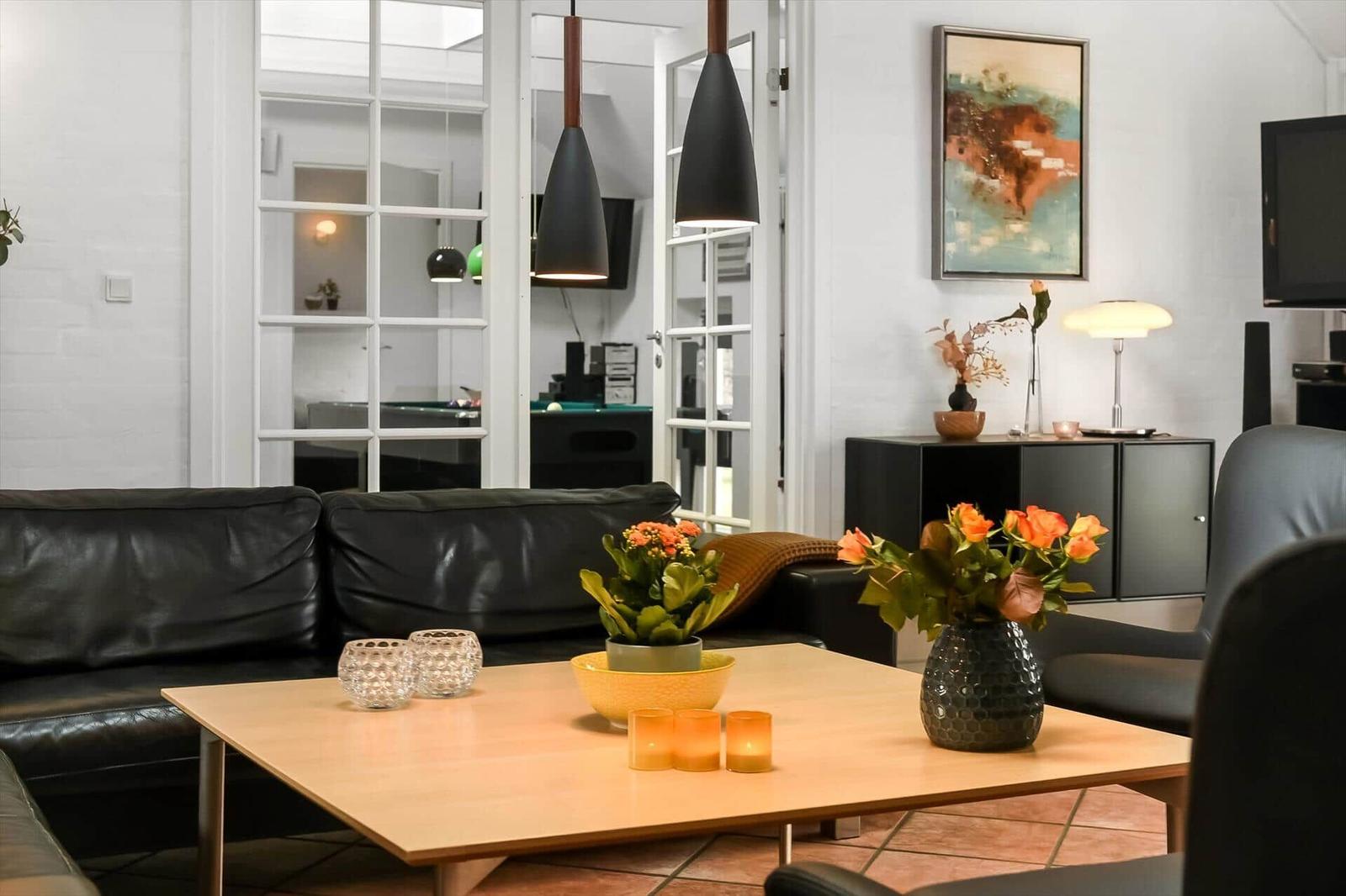 Ein Wohnzimmer mit schwarzer Ledercouch, Holztisch und dekorativen Blumen.