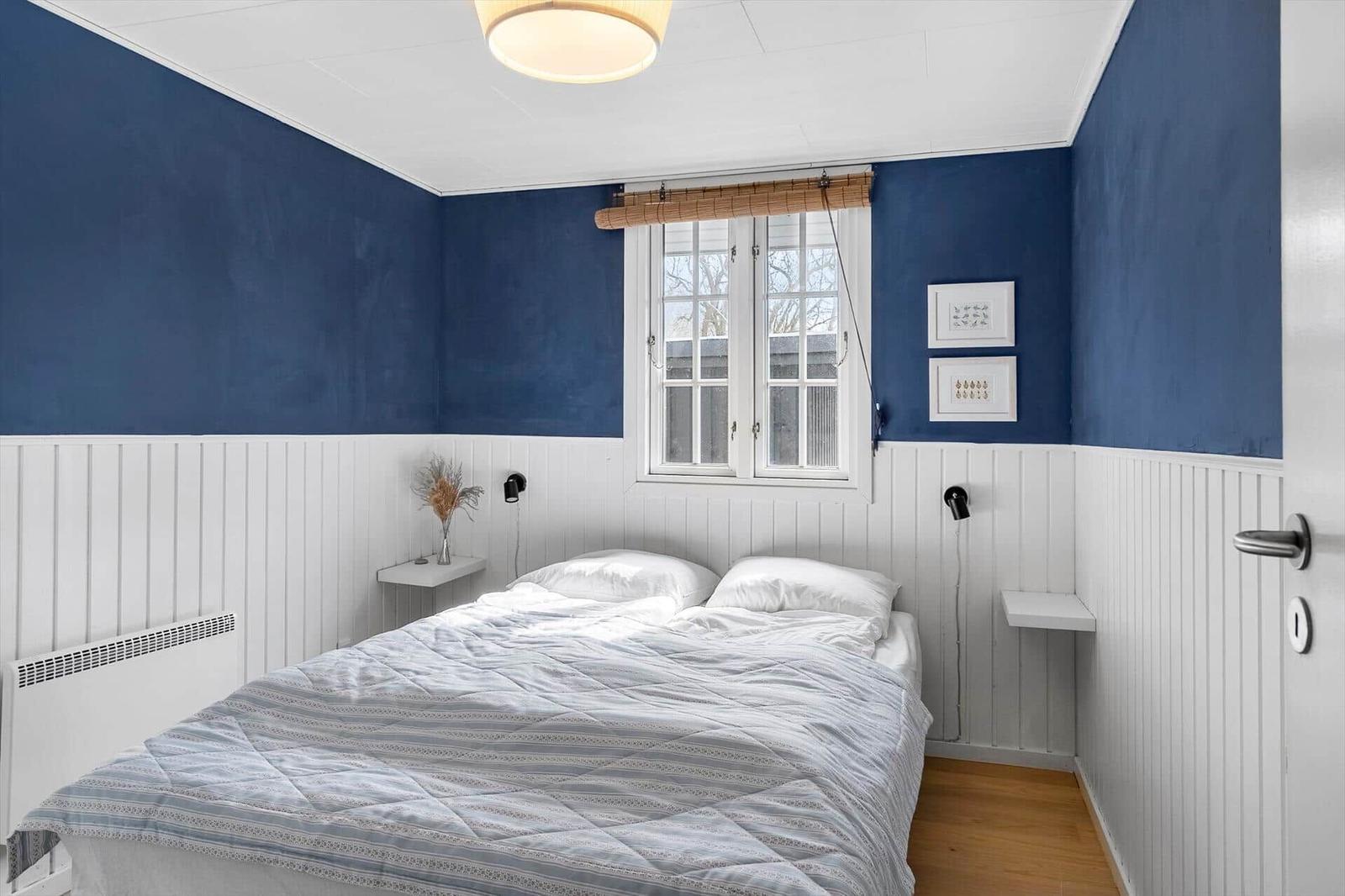 Schlafzimmer mit blauen Wänden, weißem Paneel und Doppelbett unter Fenster.