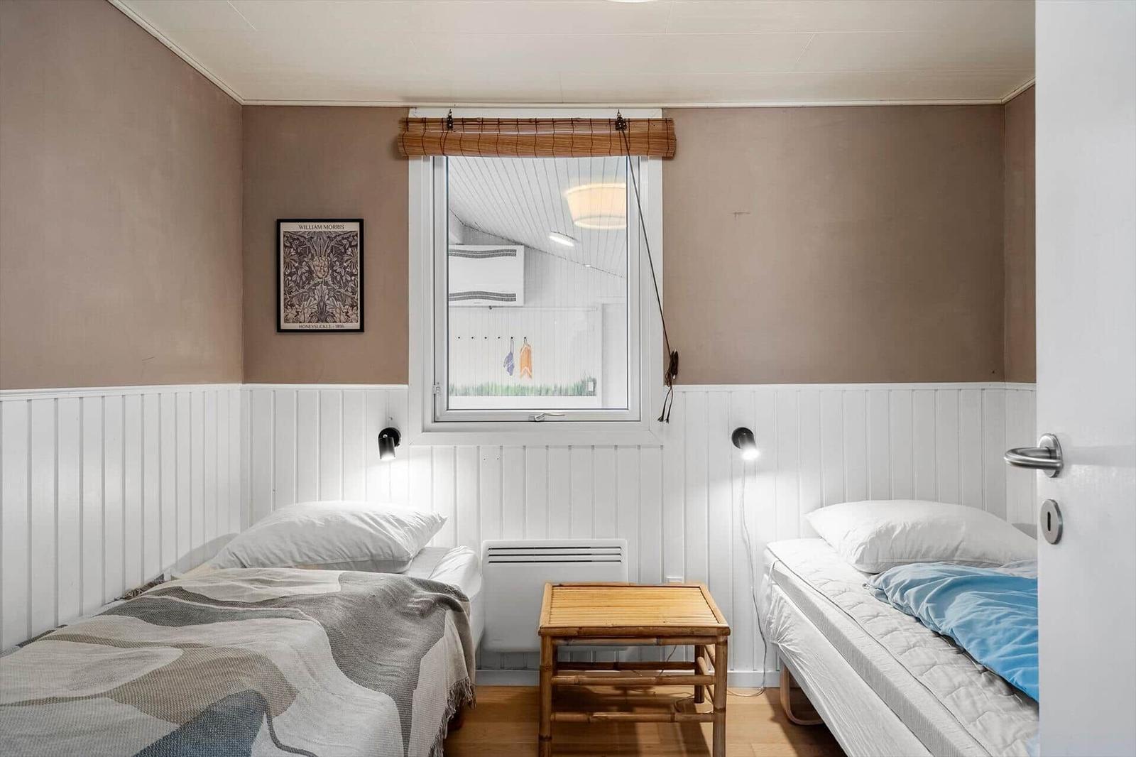 Zwei Einzelbetten mit Tisch und Fenster. Wandverkleidung und Bild an der Wand.