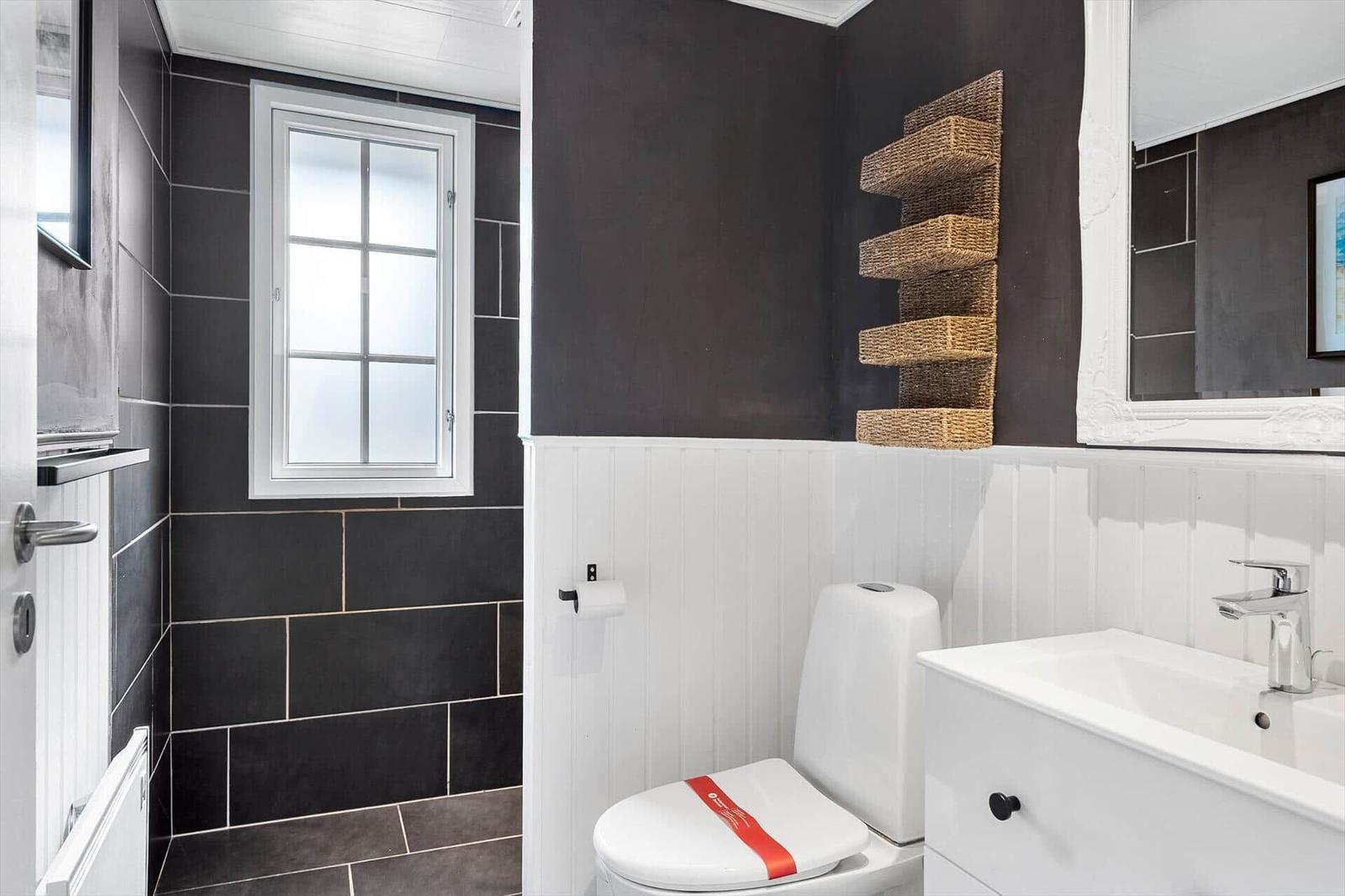 Badezimmer mit Toilette, Waschbecken und Fenster. Wandverkleidung und Wandregal.
