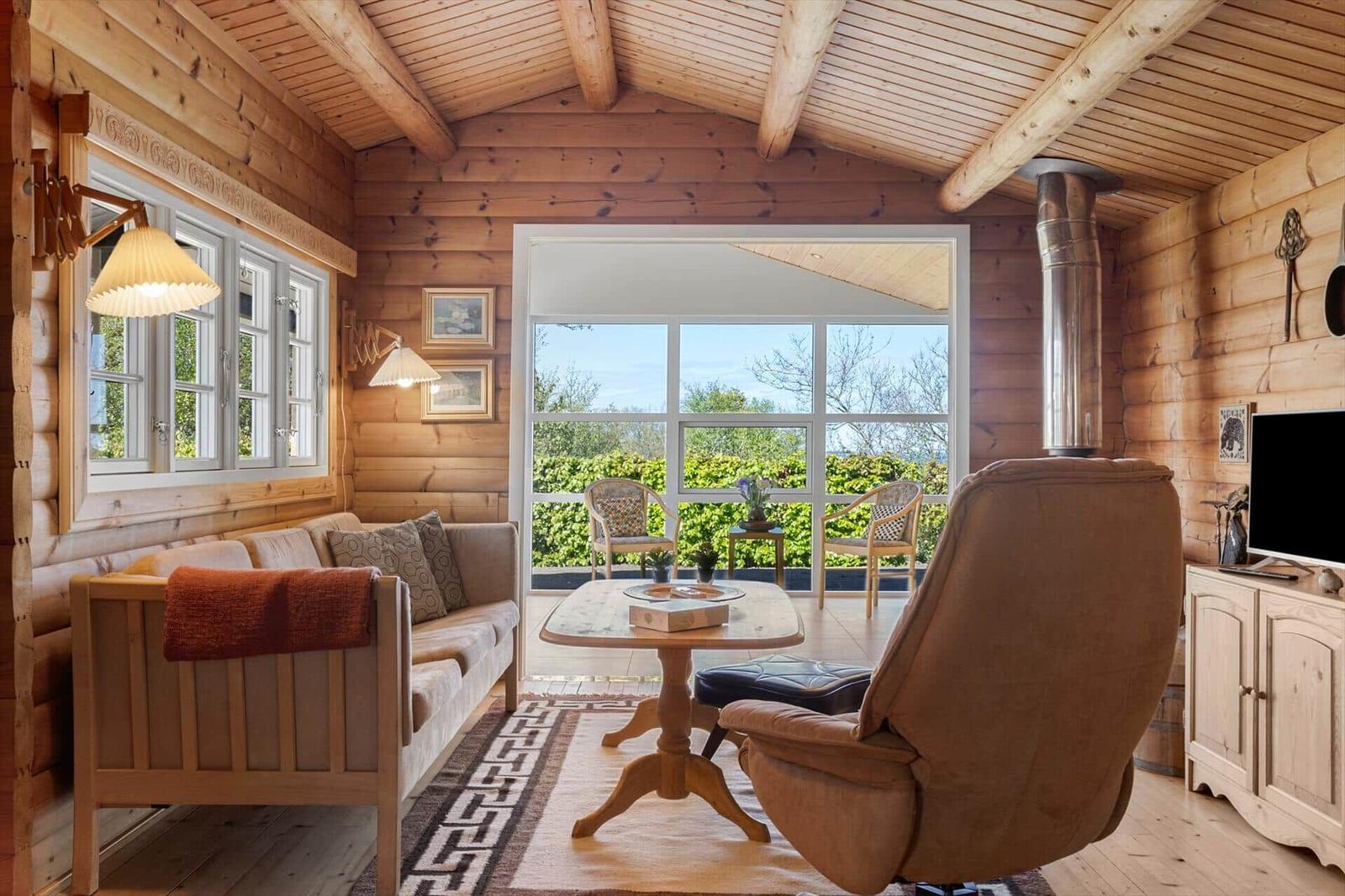Wohnzimmer mit Holzwand, Sofa, Sessel und Blick auf Balkon.
