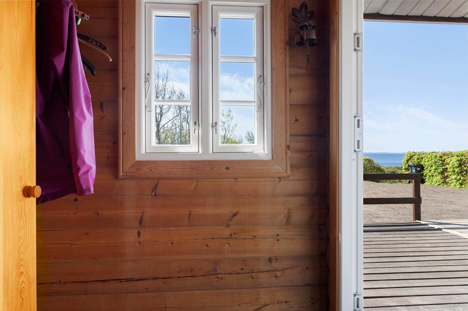 Holzhaus mit Fenster und Blick auf den See. Tür führt auf eine Terrasse.