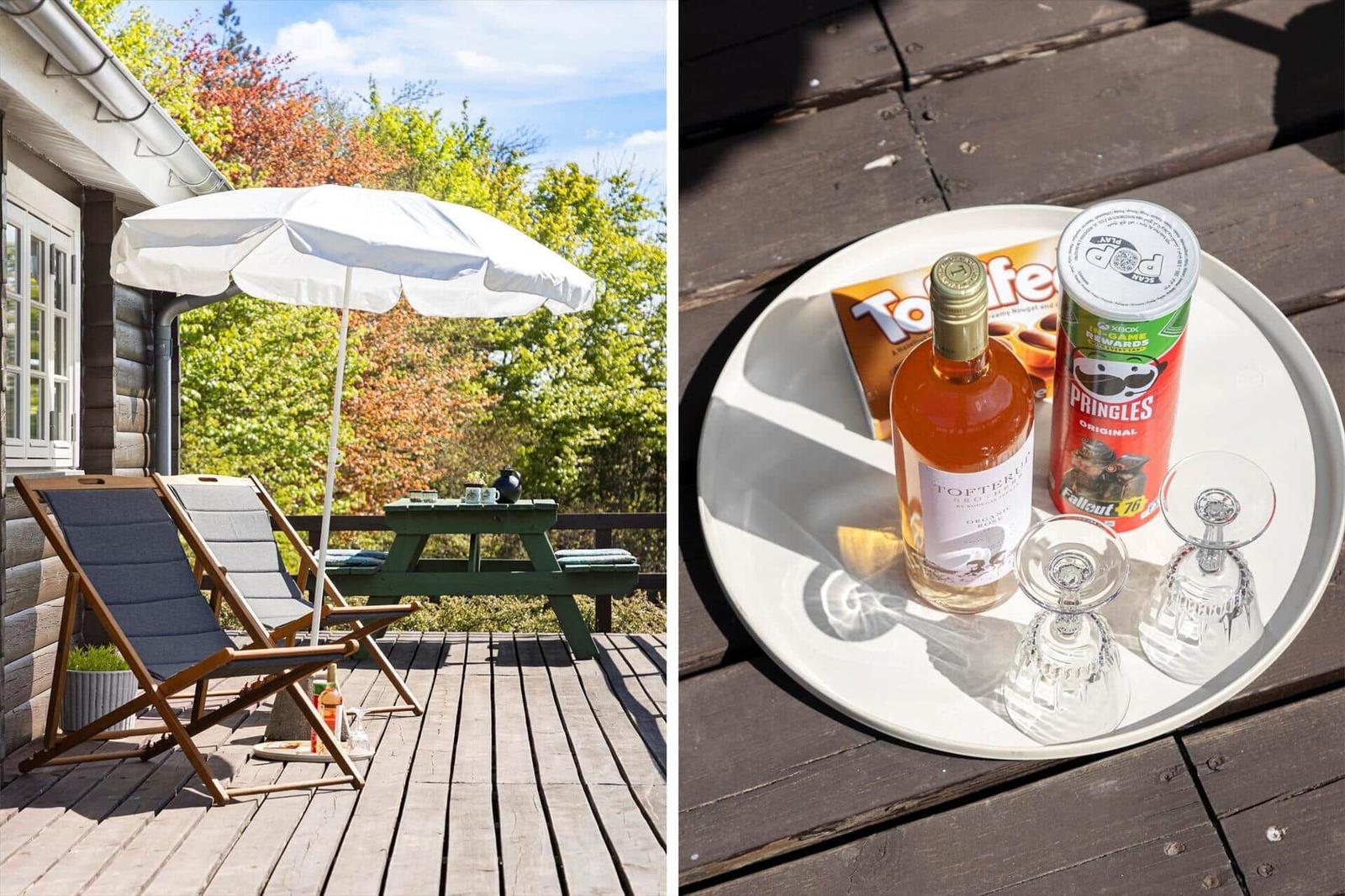 Terrasse mit Liegestühlen, Sonnenschirm und Picknicktisch. Tisch mit Wein, Snacks und Gläsern.