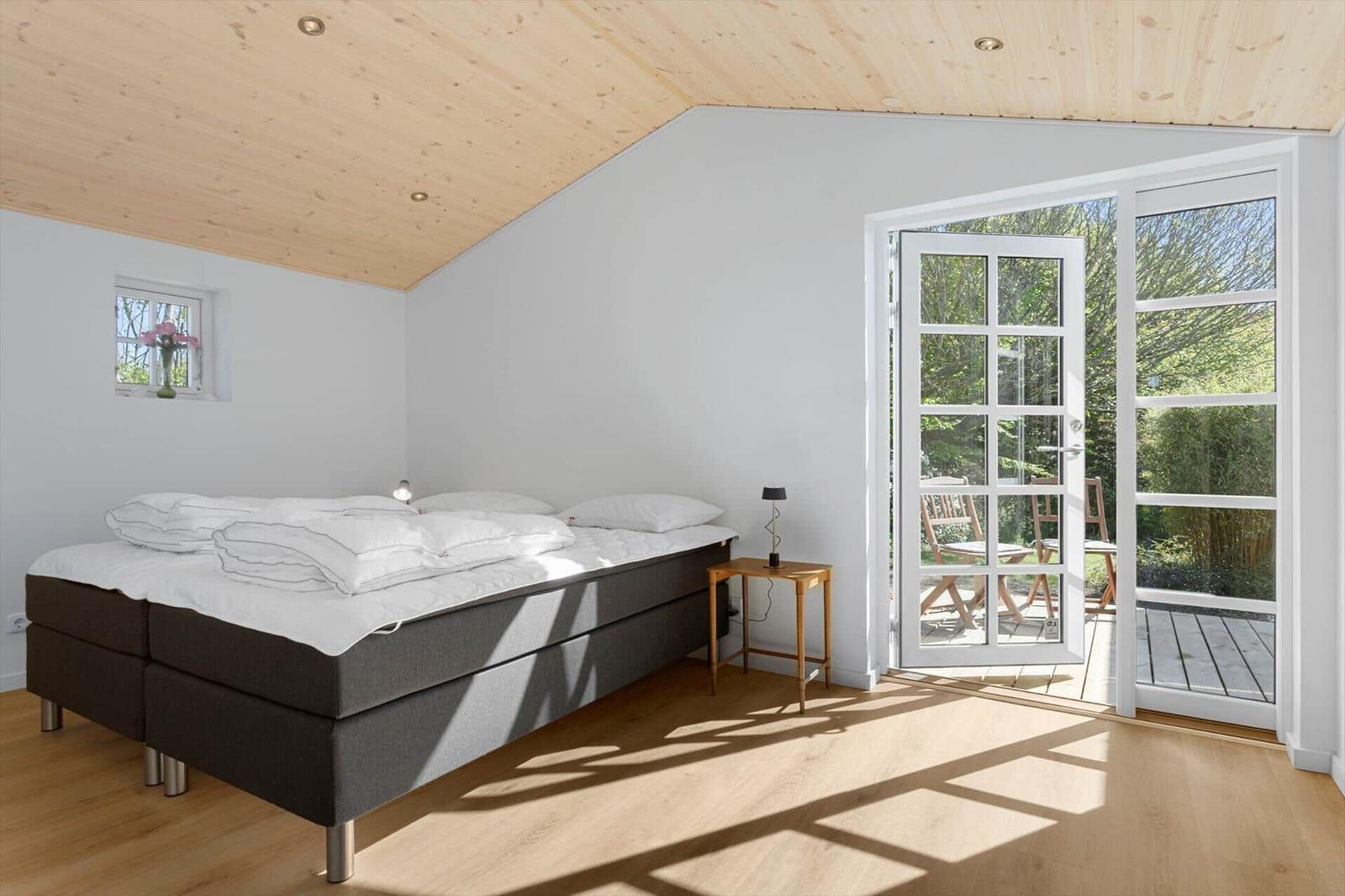 Schlafzimmer mit Bett, Fenster und Glastür zum Garten.