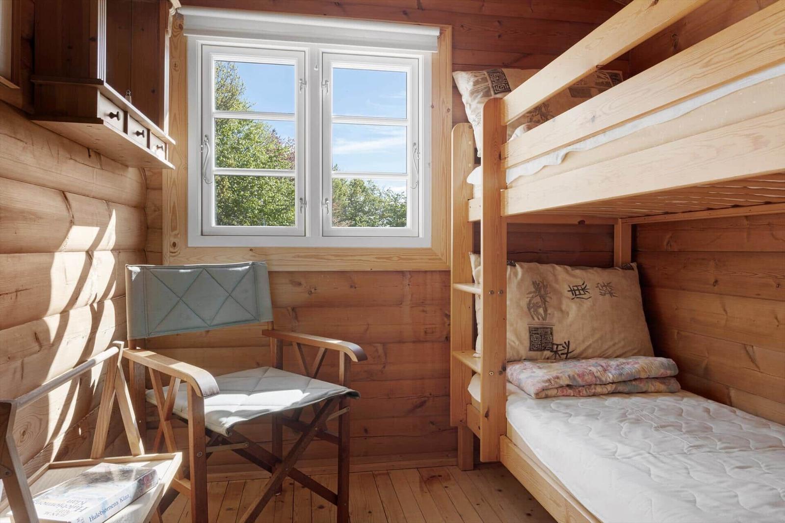 Ein Schlafzimmer mit Holzwand, Doppelstockbett und Fenster mit Blick auf Bäume.