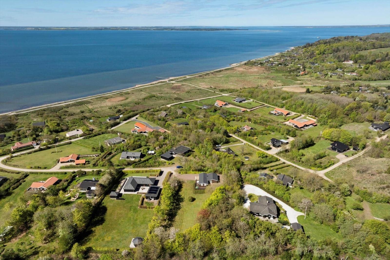 Luftbild einer Küstenlandschaft mit mehreren Häusern und grünen Flächen am Wasser.