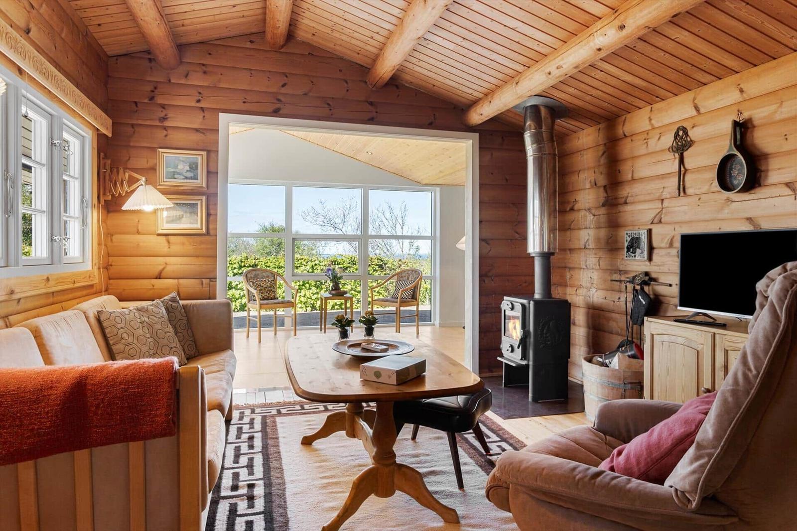 Wohnzimmer mit Holzwand, Kamin und Sitzgelegenheiten. Durchgang zum Balkon mit Blick.