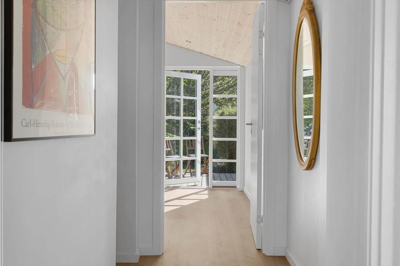 Hallen mit Holzboden und Fenster zur Terrasse. Wandbild und runder Spiegel.