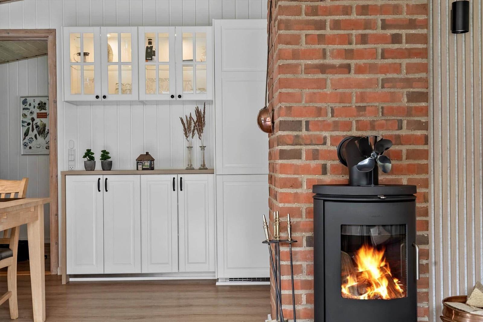 Kamin mit brennendem Holz, weiße Schränke und Backsteinwand im Wohnbereich.