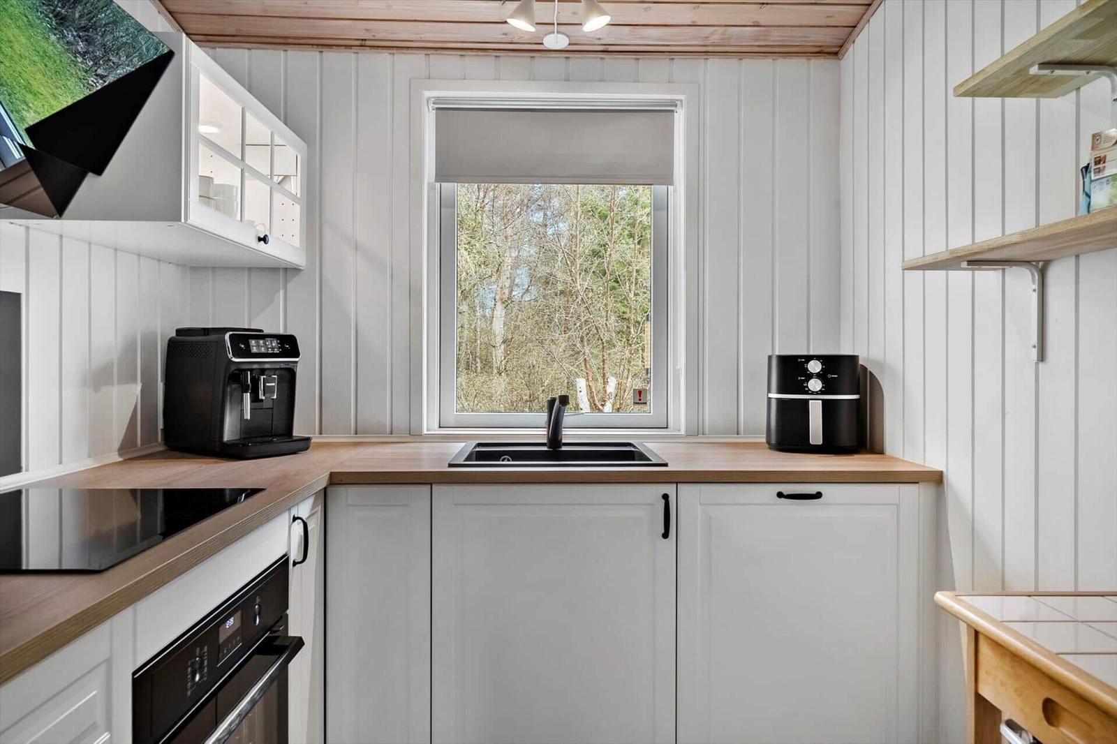Küche mit Fenster, Spüle, Kaffeemaschine und Airfryer. Holzoberflächen und weiße Schränke.