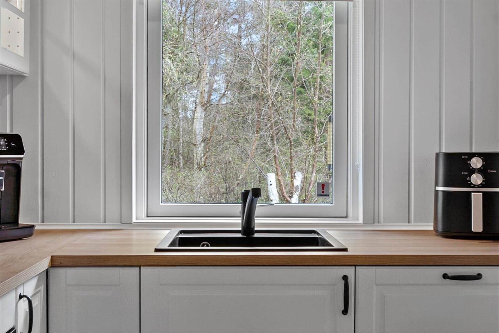 Küche mit Holzoberfläche, Waschbecken und Fensterblick auf Wald.