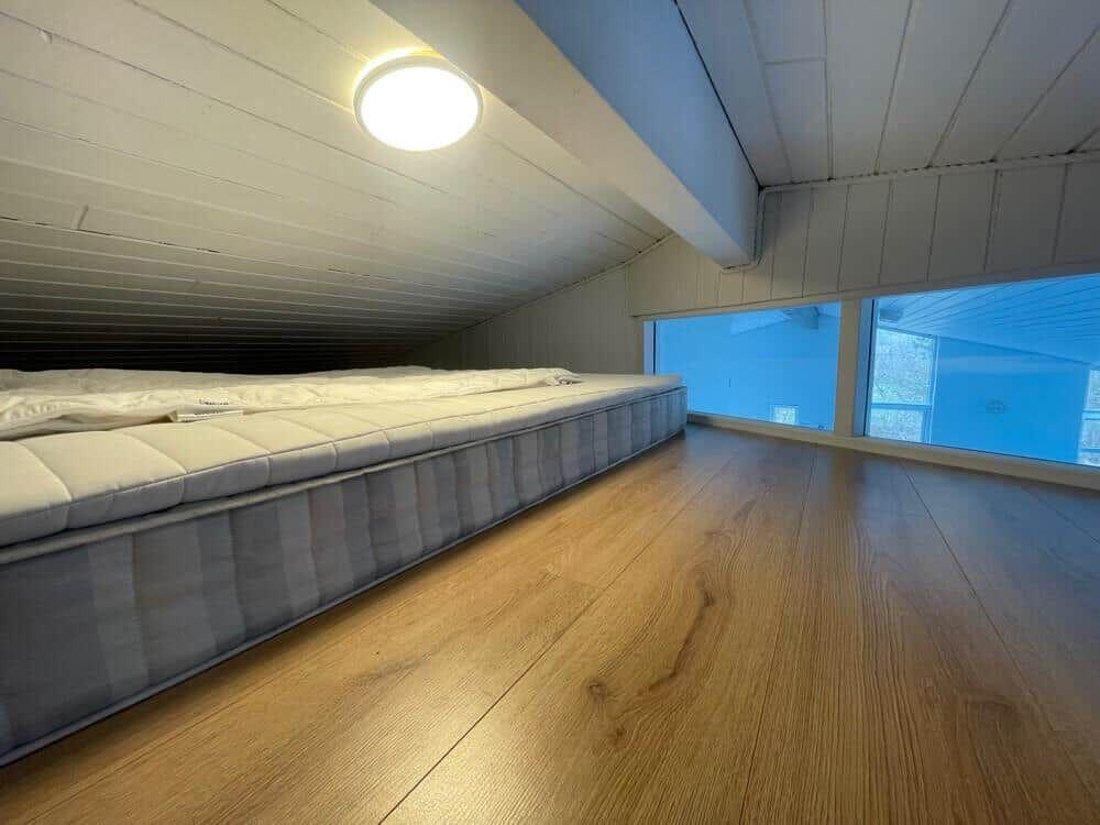 Schlafzimmer mit Matratze auf Holzboden und großem Fenster