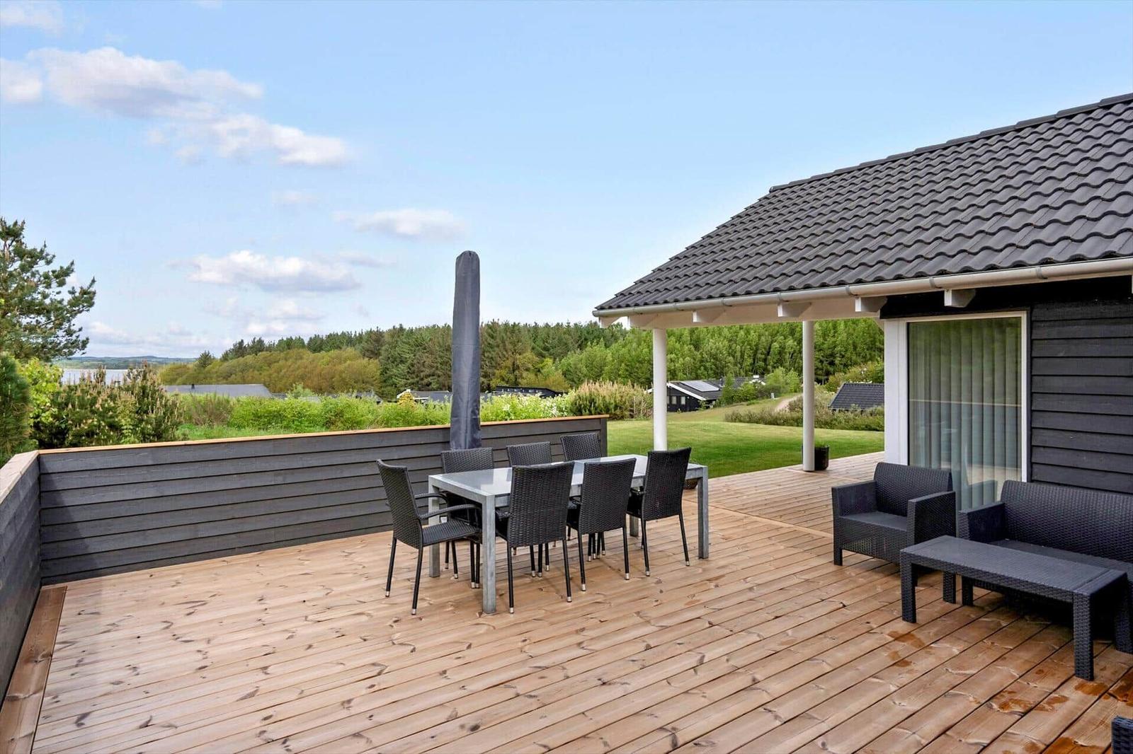 Terrasse mit Tisch, Stühlen und Sitzgruppe. Blick auf Wald und Grünflächen.