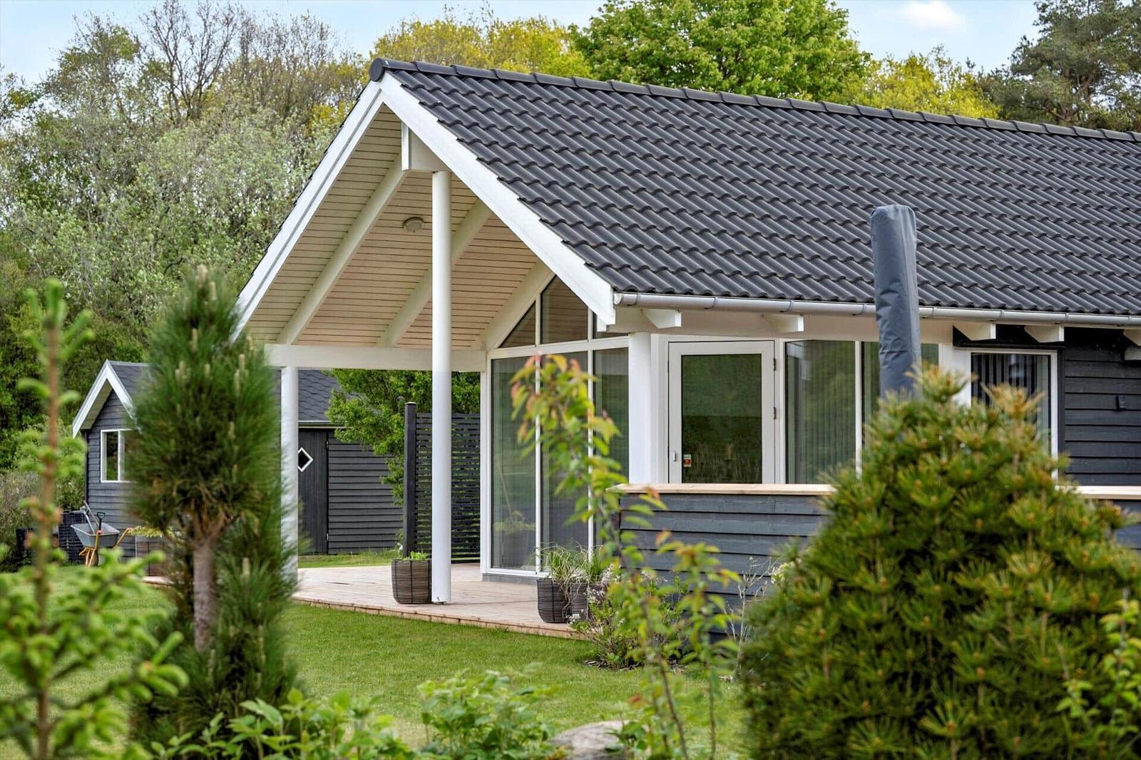 Moderne Villa mit Holzterrasse und großem Fensterbereich im Grünen.