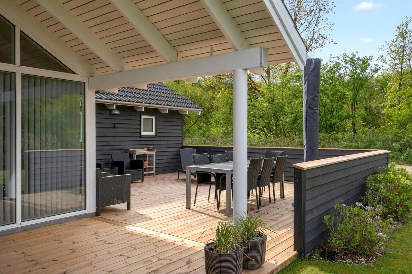 Terrasse mit Tisch und Stühlen, Holzboden und Sicht auf grüne Umgebung.