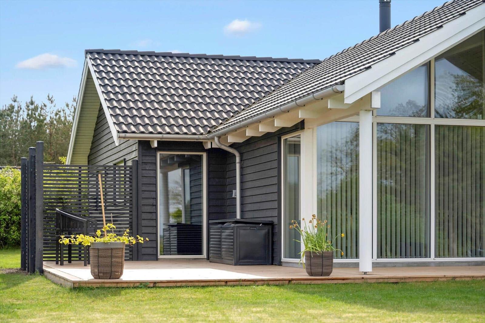 Moderne Ferienwohnung mit Terrasse, großen Fenstern und Pflanzen im Vorgarten.