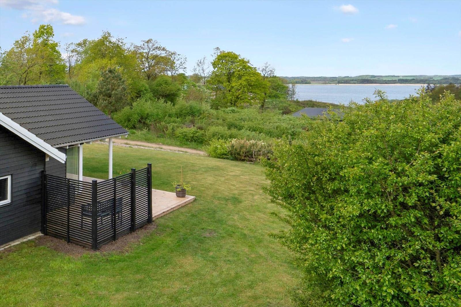 Schwarzes Haus mit Terrasse, Grünfläche und Blick auf Wasser.