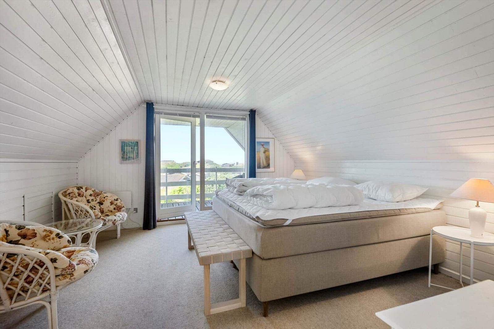 Bedroom with sloped ceiling, bed, seating, and balcony door.