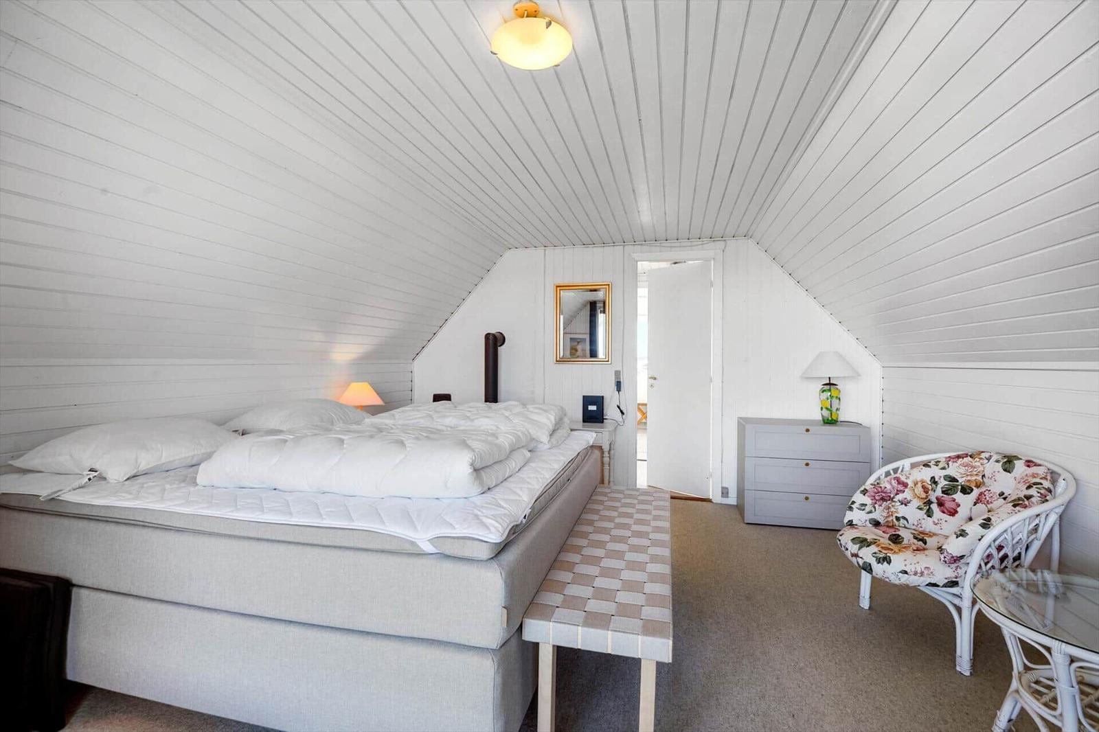 Bedroom with bed, chair, and dresser under sloped ceilings.