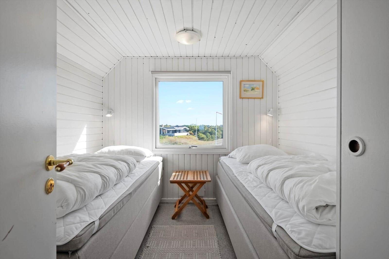Two beds in a room with white wood paneling and window view.